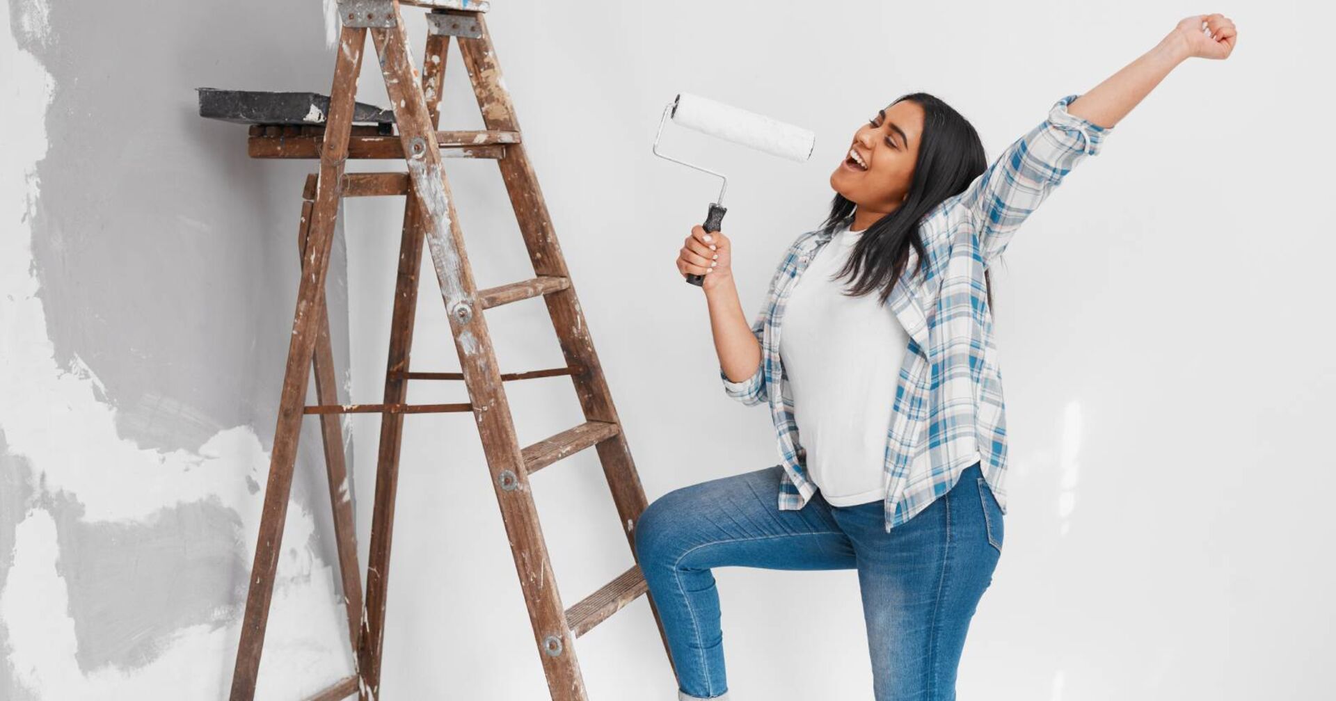 Junge Frau auf der Leiter, die symbolisch die Farbrolle als Mikrofon nimmt und darin &quot;singt&quot;.