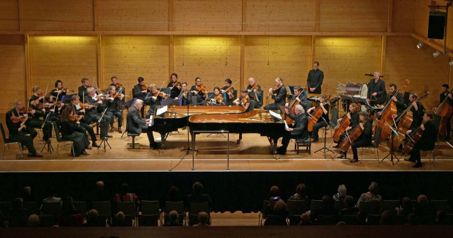 Orchester mit Pianisten, Chello- und Geigenspieler vor einem Publikum
