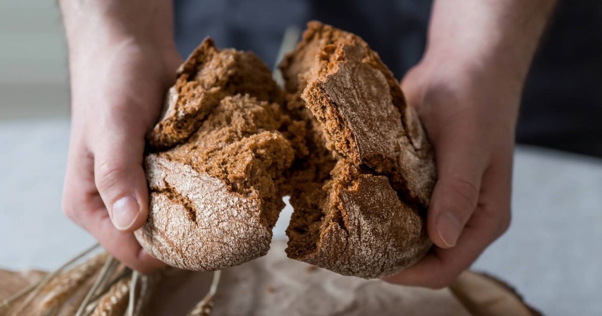 Detailansicht eines Brotes, das gerade von Hand in der Mitte gebrochen wird.