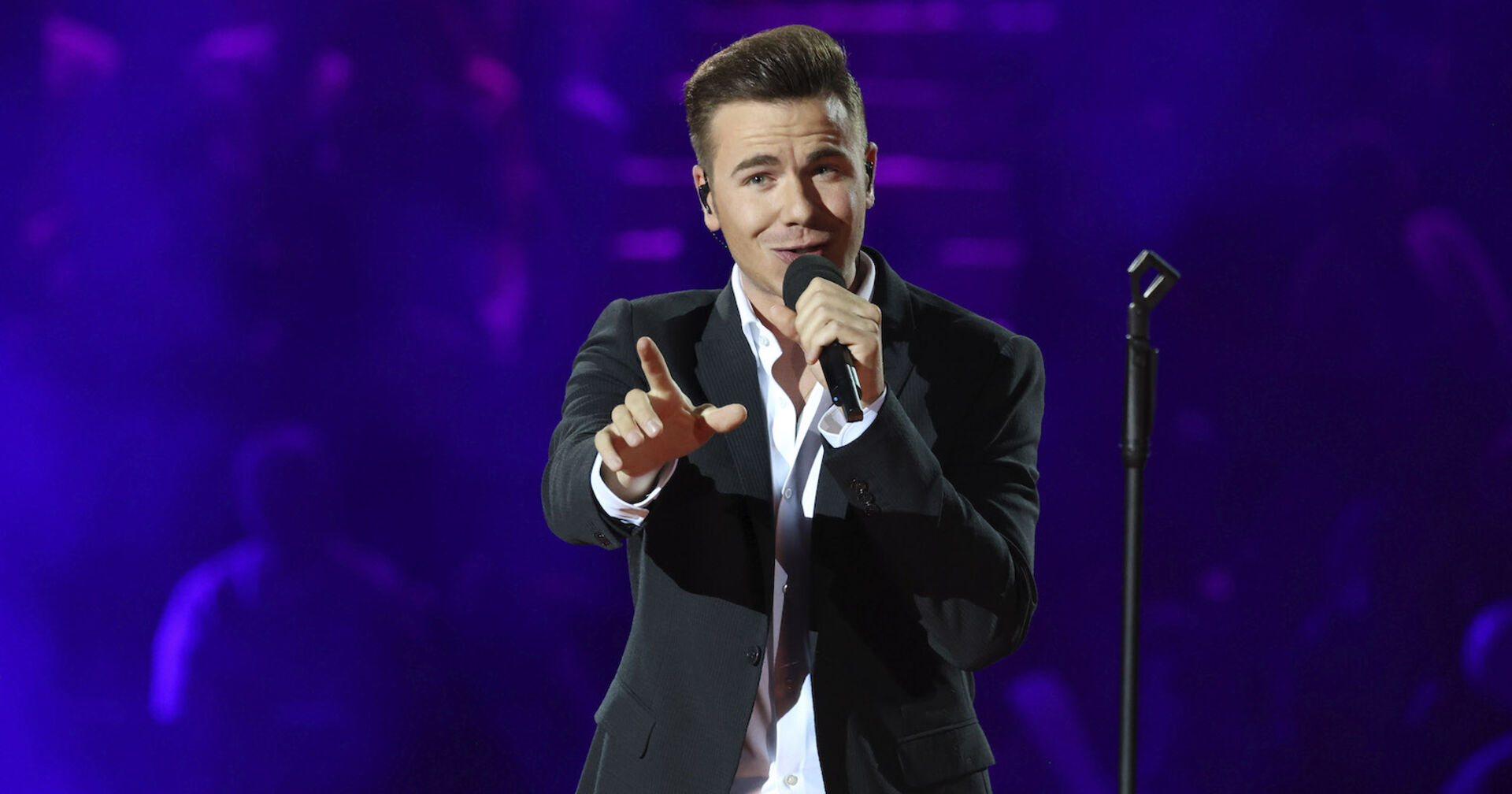 Eric Philipp mit einem Sakko auf der Bühne und einem Mikrofon in der Hand.