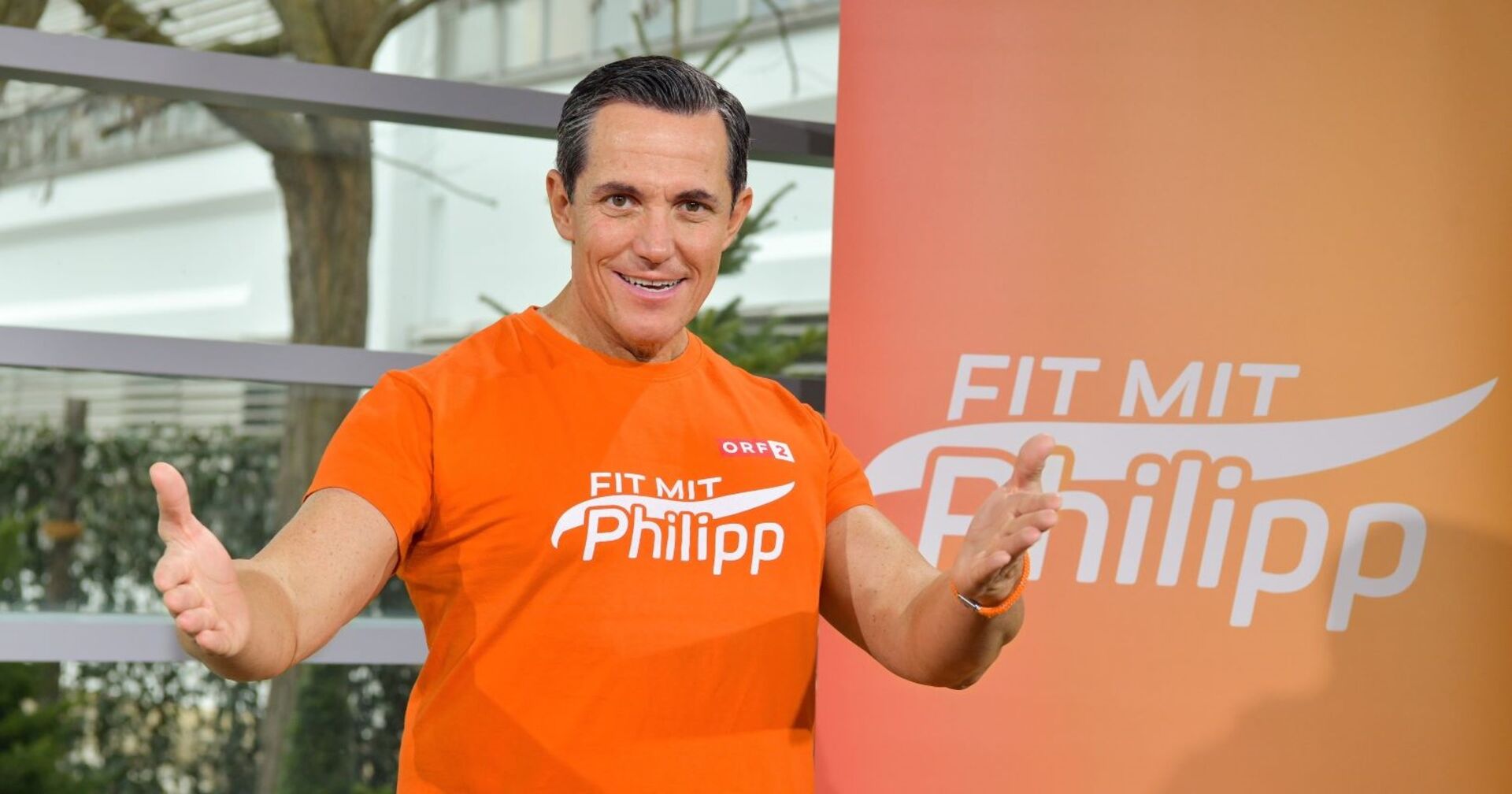 Philipp Jelinek in seine Fitness-Dress vor einem Banner mit der Aufschrift &quot;Fit mit Philipp&quot;
