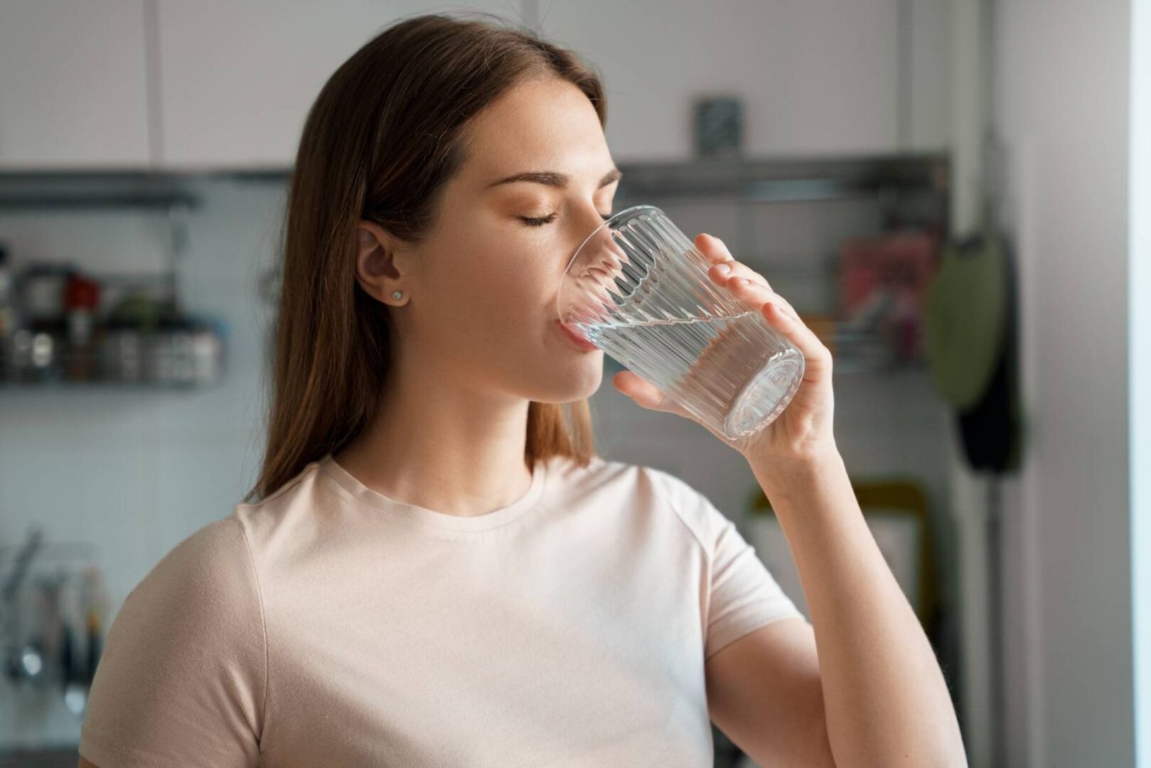 Junge Frau, die gerade von einem Glas mit Wasser trinkt.