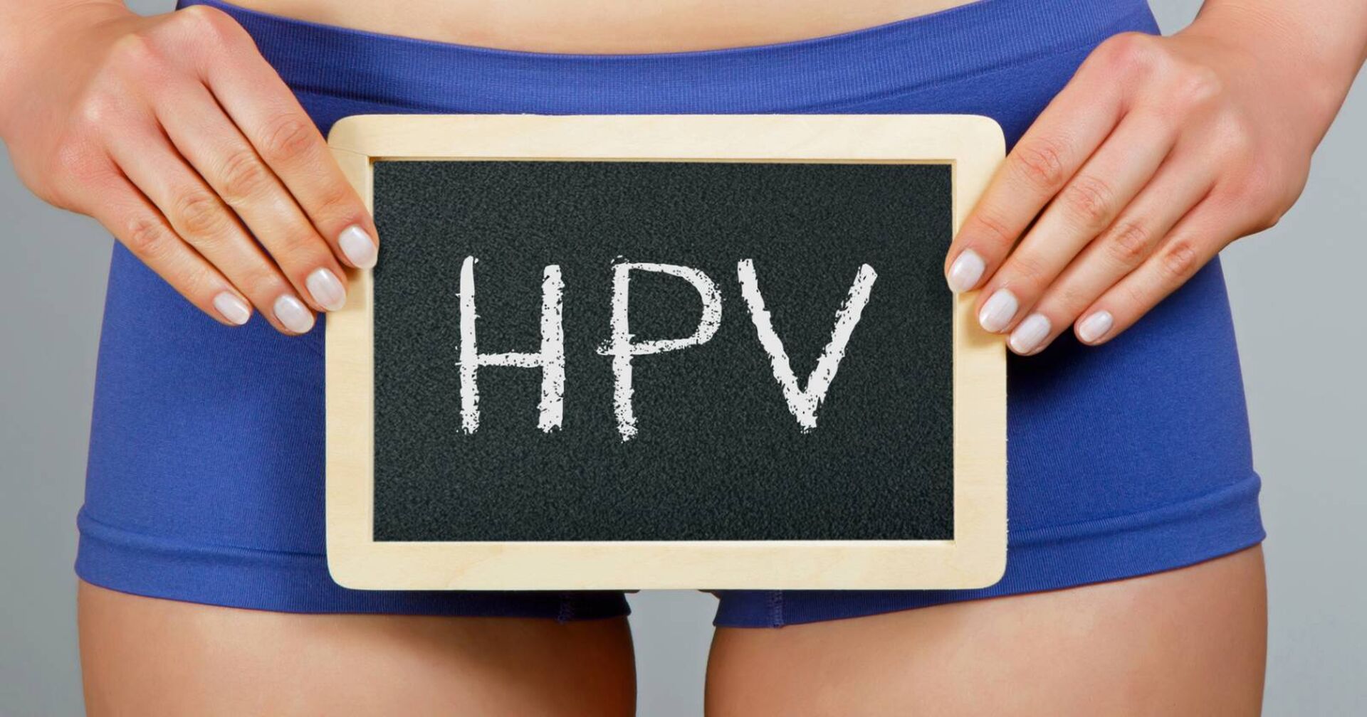 Junge Frau die in der Höhe ihrer Hüfte eine beschriebene Tafel mit der Abkürzung 'HPV' hält