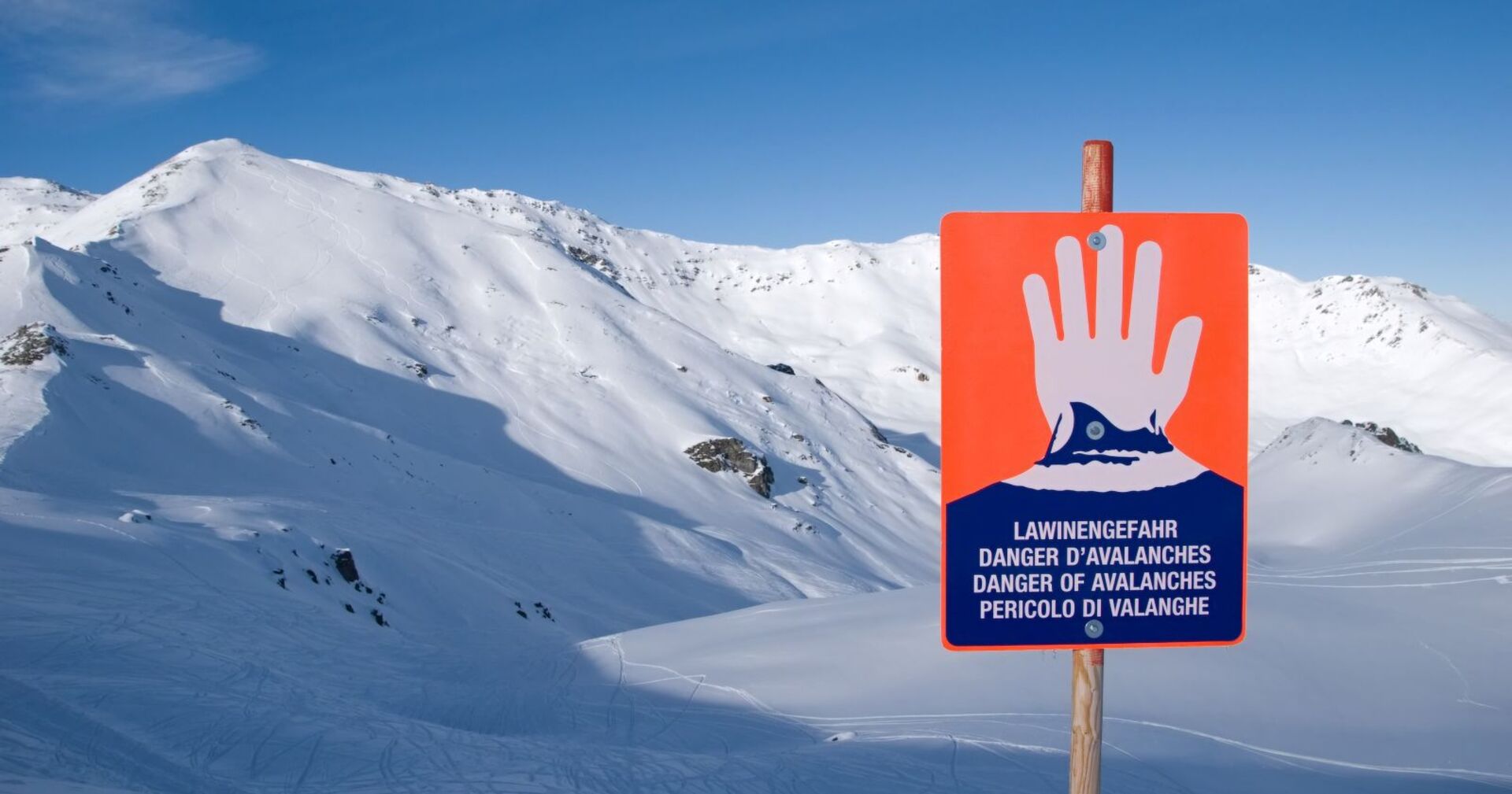 Hinweisschild für Lawinengefahr vor verschneiten Bergen.