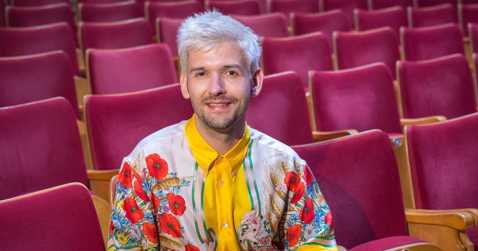 Michi Buchinger mit einem bunten T-Shirt auf einer Sitzreihe.