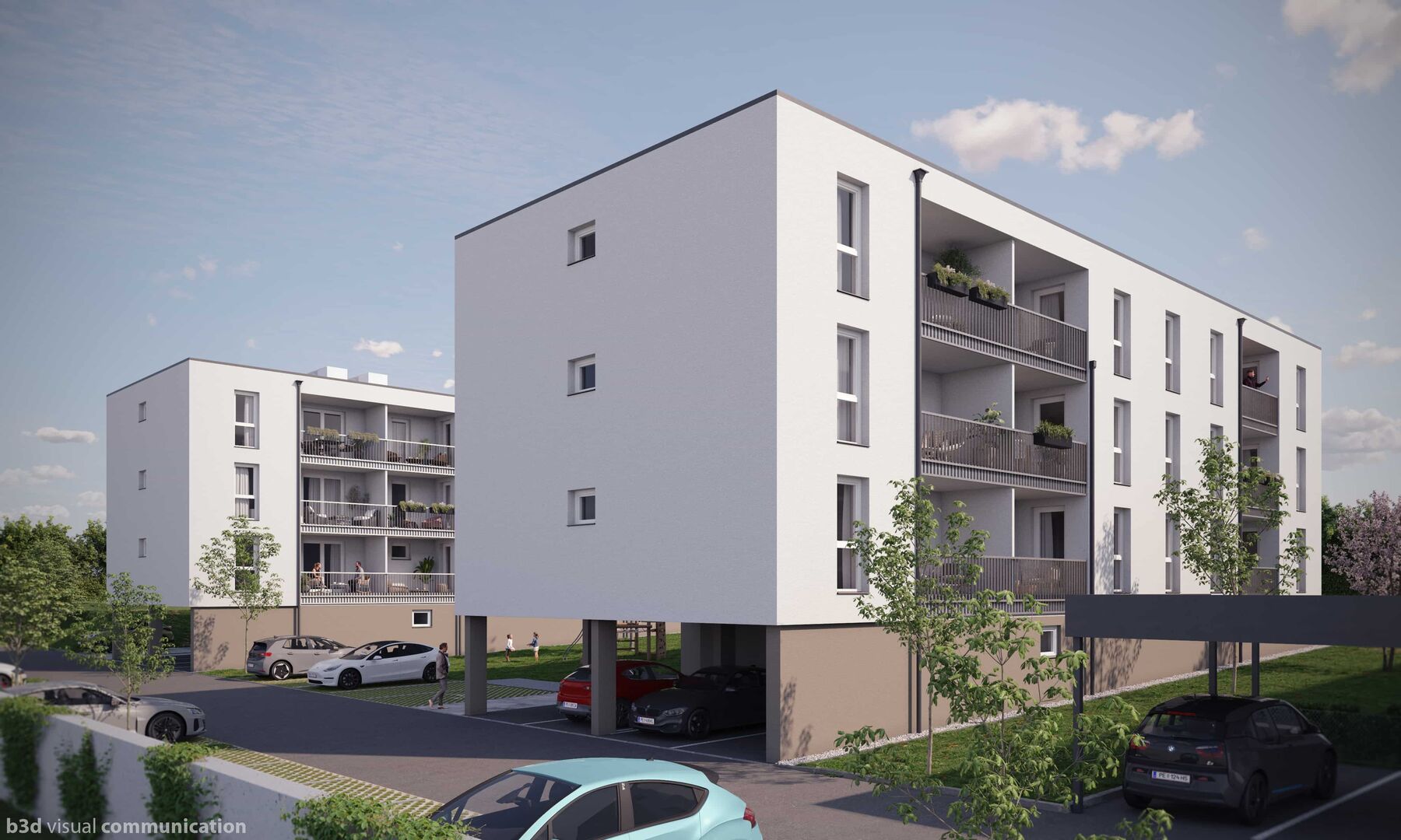 Zwei weiße Wohnblöcke stehen im Grünen. Die Häuser sind umgeben von Laubbäumen und Menschen. Auch einige Autos parken hier.