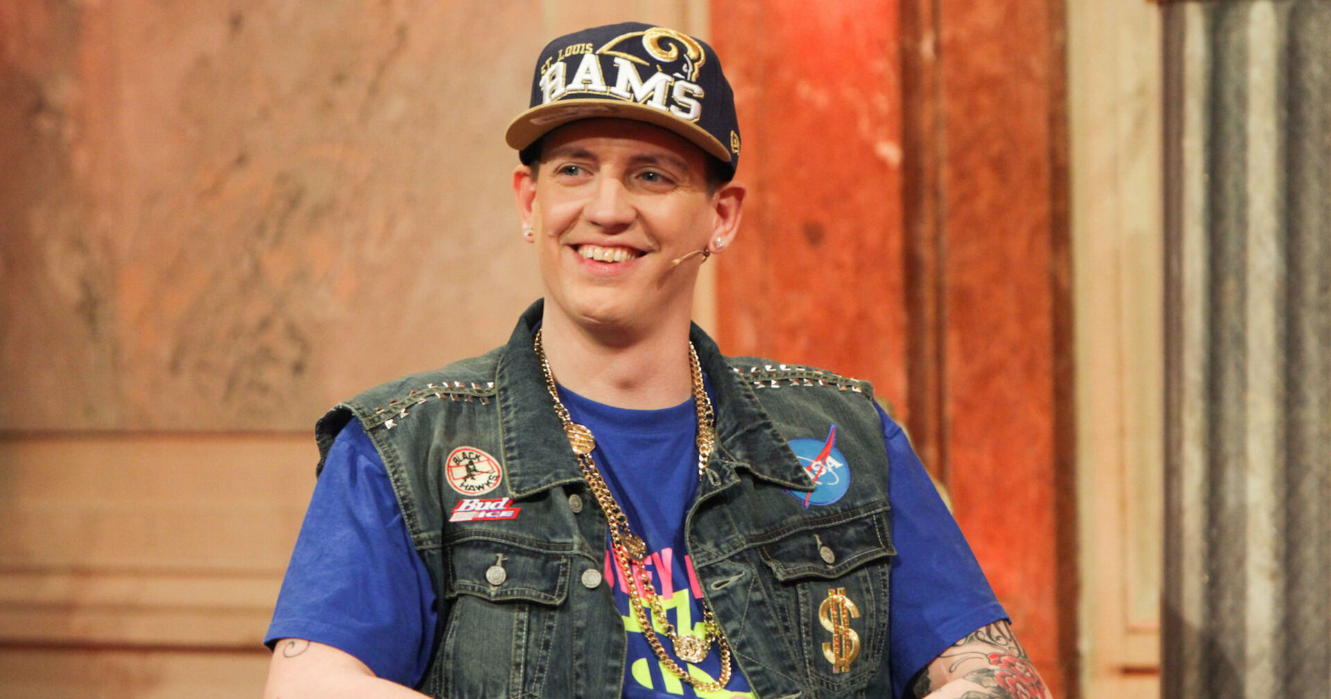 Money Boy mit einer großen Kappe und einer Jacke mit Sticker bei &quot;Wir sind Kaiser&quot;.