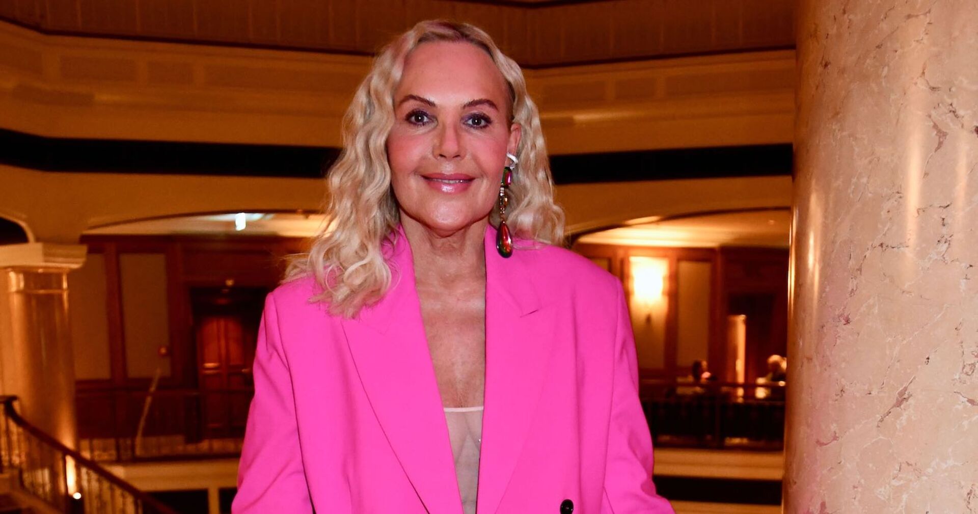 Natascha Ochsenknecht mit einem pinken Outfit und offenen blonden gewellten Haaren.