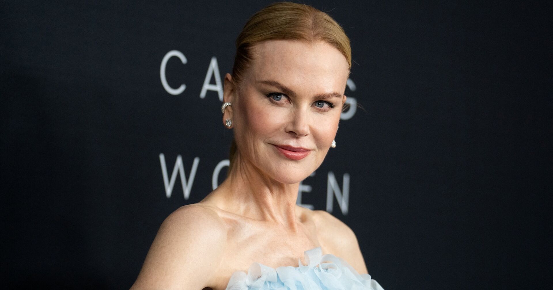 Nicole Kidman mit einem strengen Zopf vor einer schwarzen Leinwand auf dem Red Carpet.