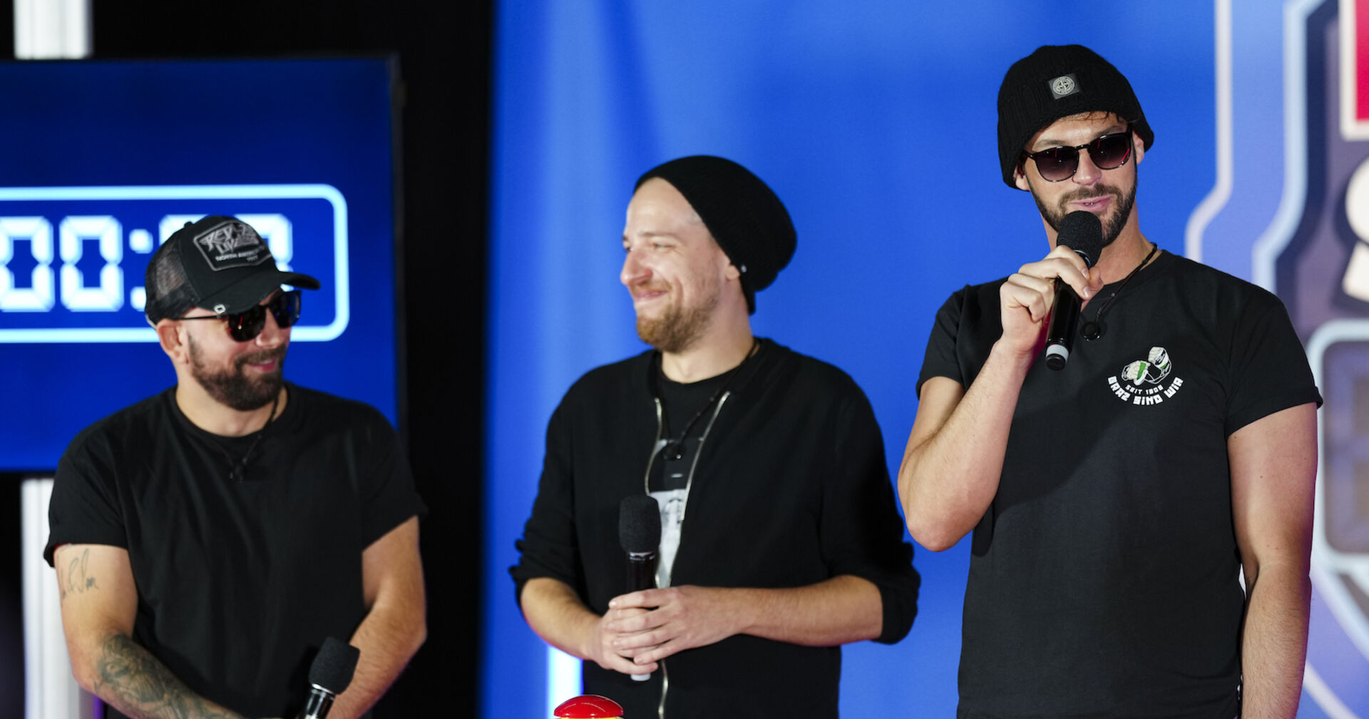 Aut of Orda auf einer Bühne mit Mikrofonen, Mützen und schwarzen Outfits.