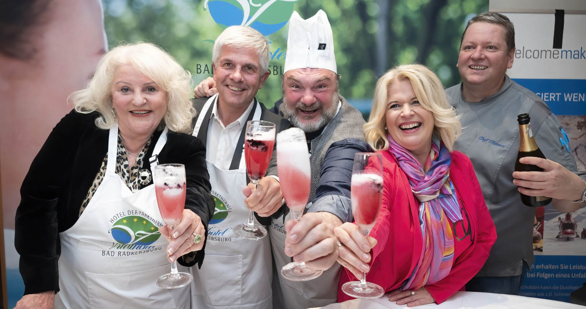 Mehrere Damen und Herren prosten mit Sektgläsern an und lachen herzhaft