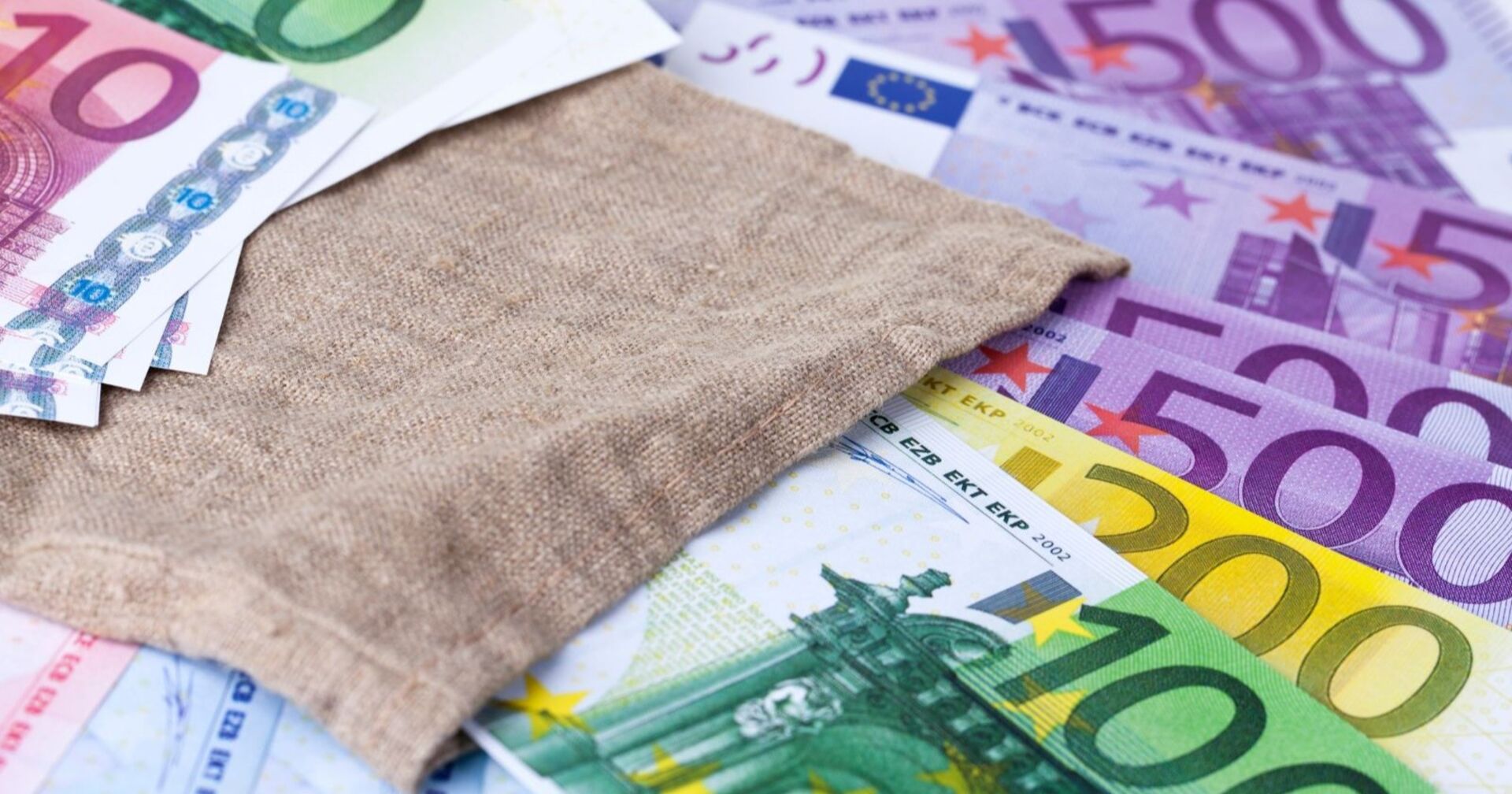 Euro-Noten auf einem Tisch, darüber ein Jutesack.