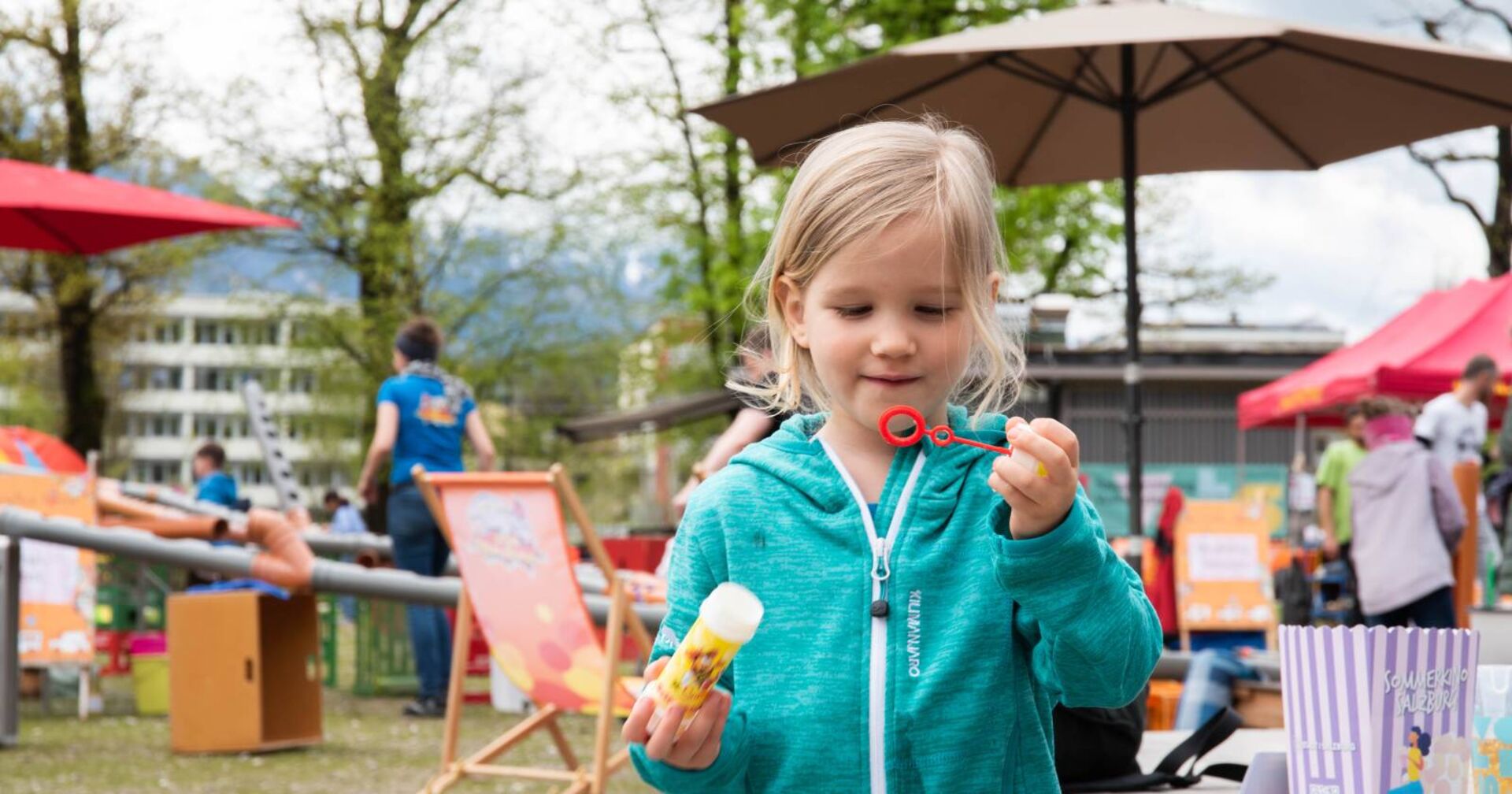Kleines Mädchen mit türkisfarbener Jacke, Seifenblasen pustend