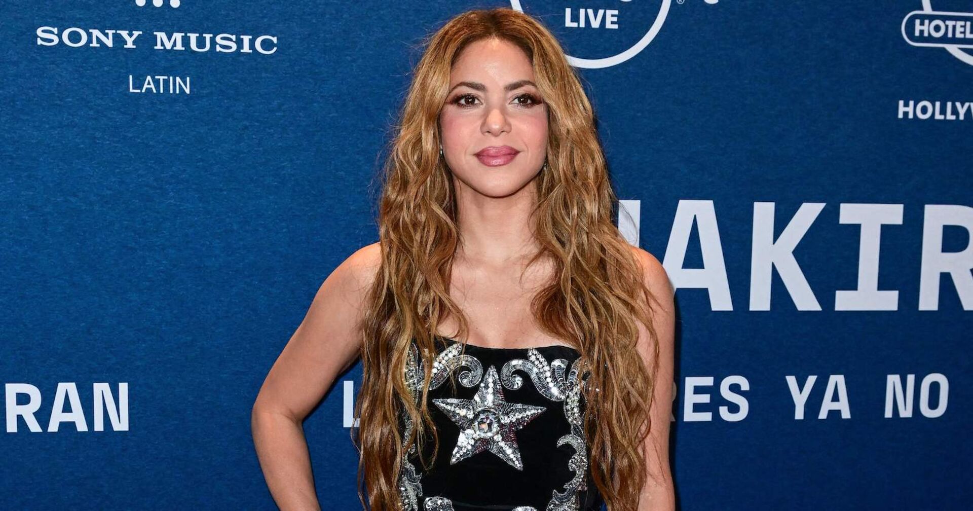 Shakira mit langen, offenen Haaren vor einer blauen Fotowand.