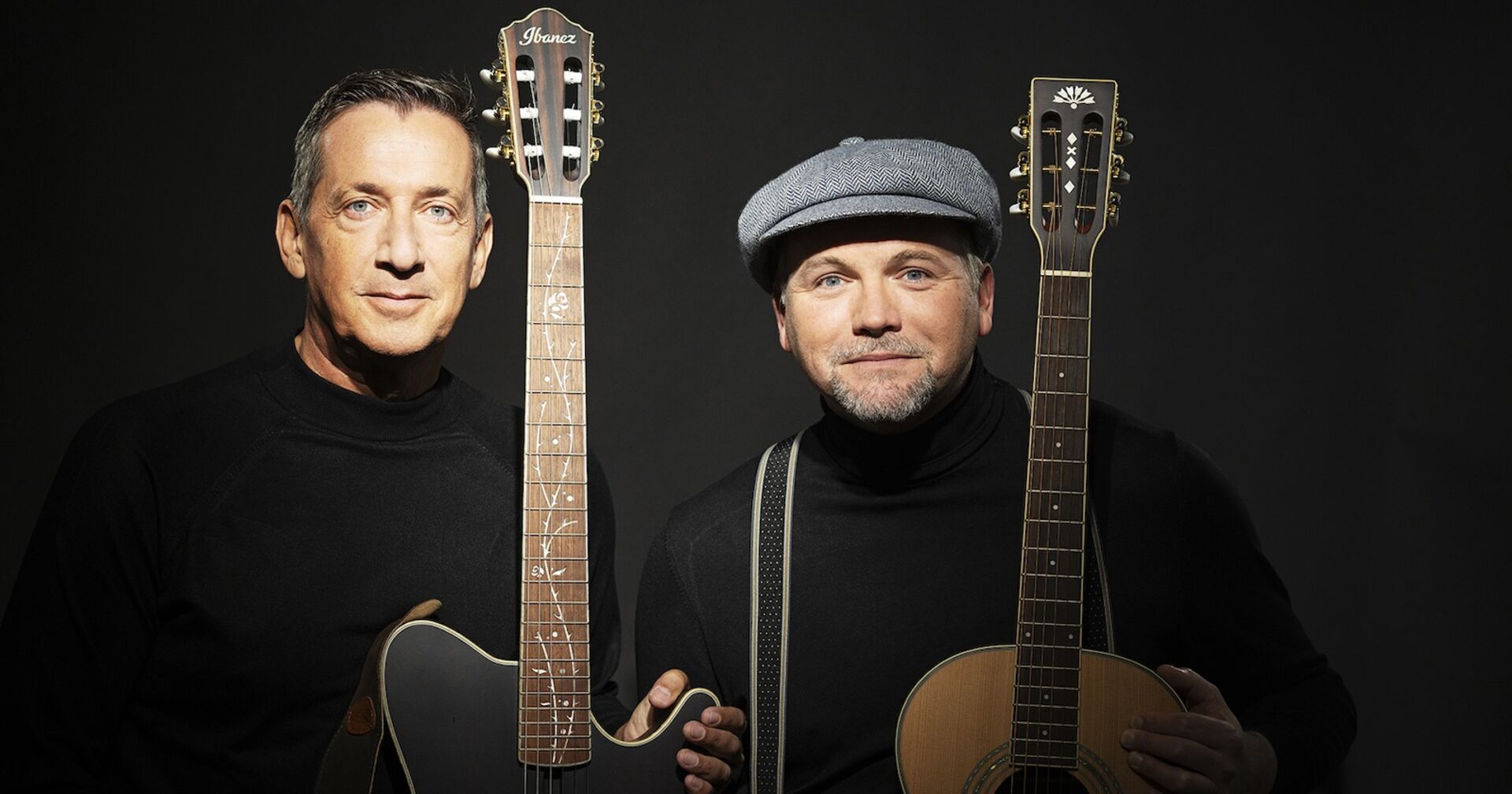 Gernot und Stipsits mit zwei Gitarren vor einem schwarzen Hintergrund.