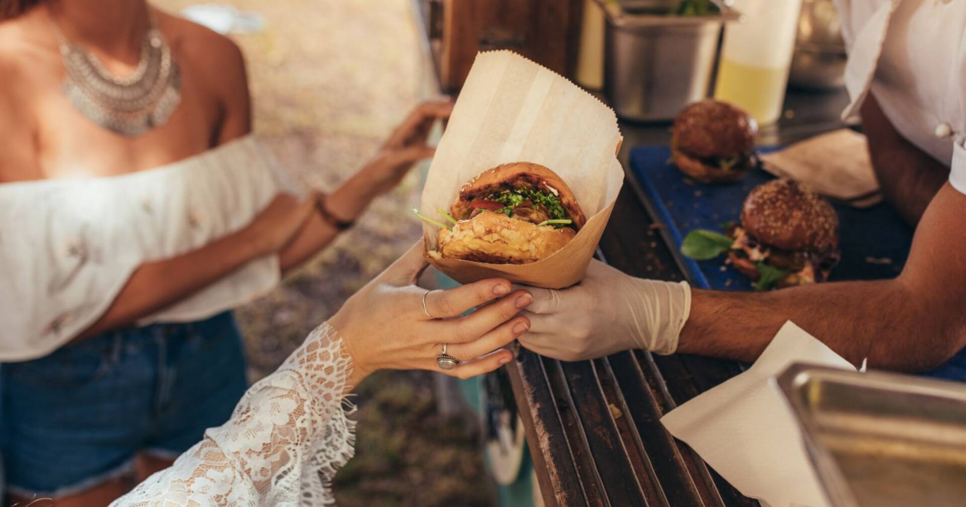 Frauenhand greift bei einem Foodtruck nach einem Burger.
