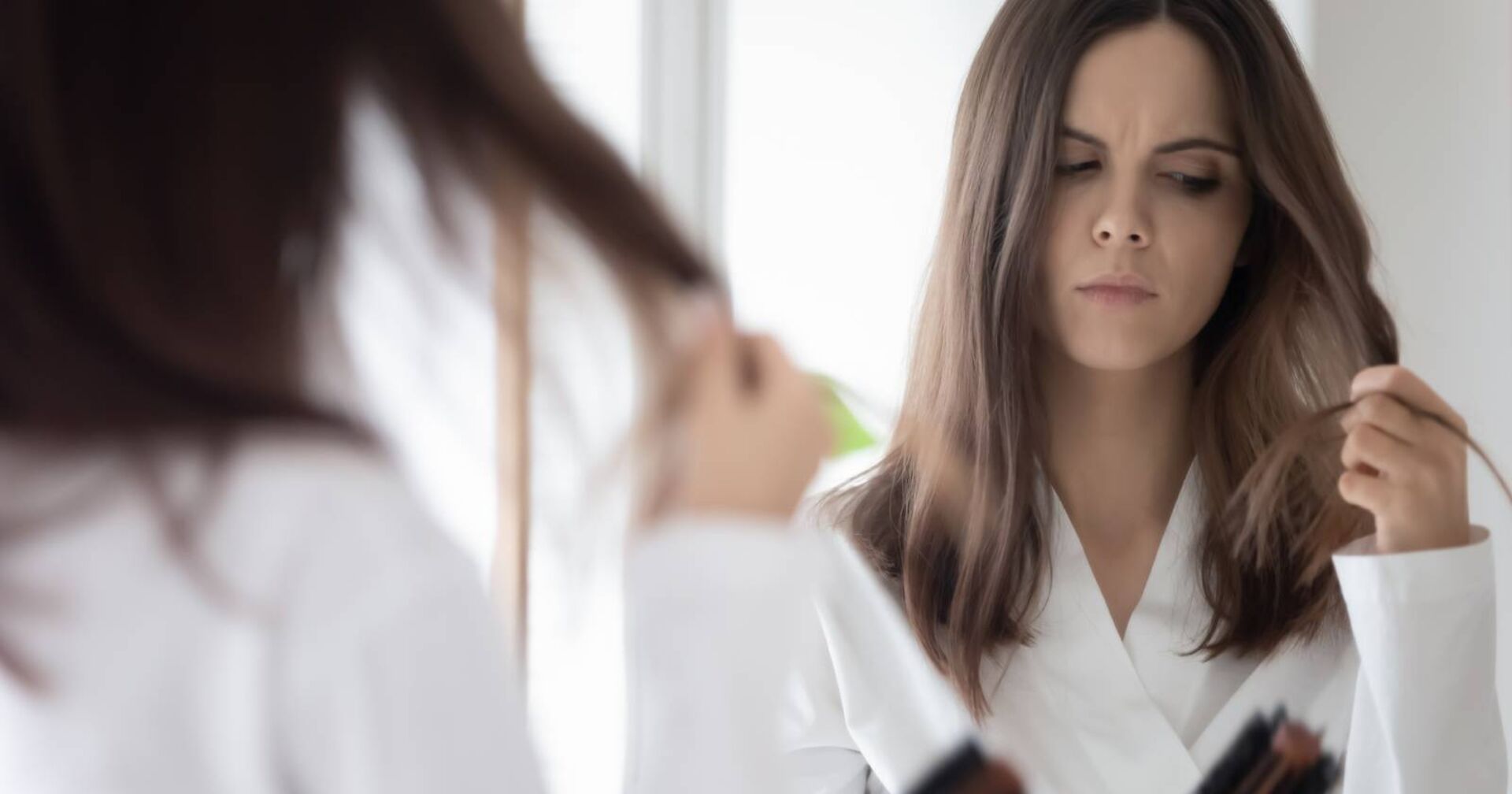 Besorgte junge Frau, die sich über die Dichte ihres Haares Gedanken macht, weil sie Haarausfall vermutet.