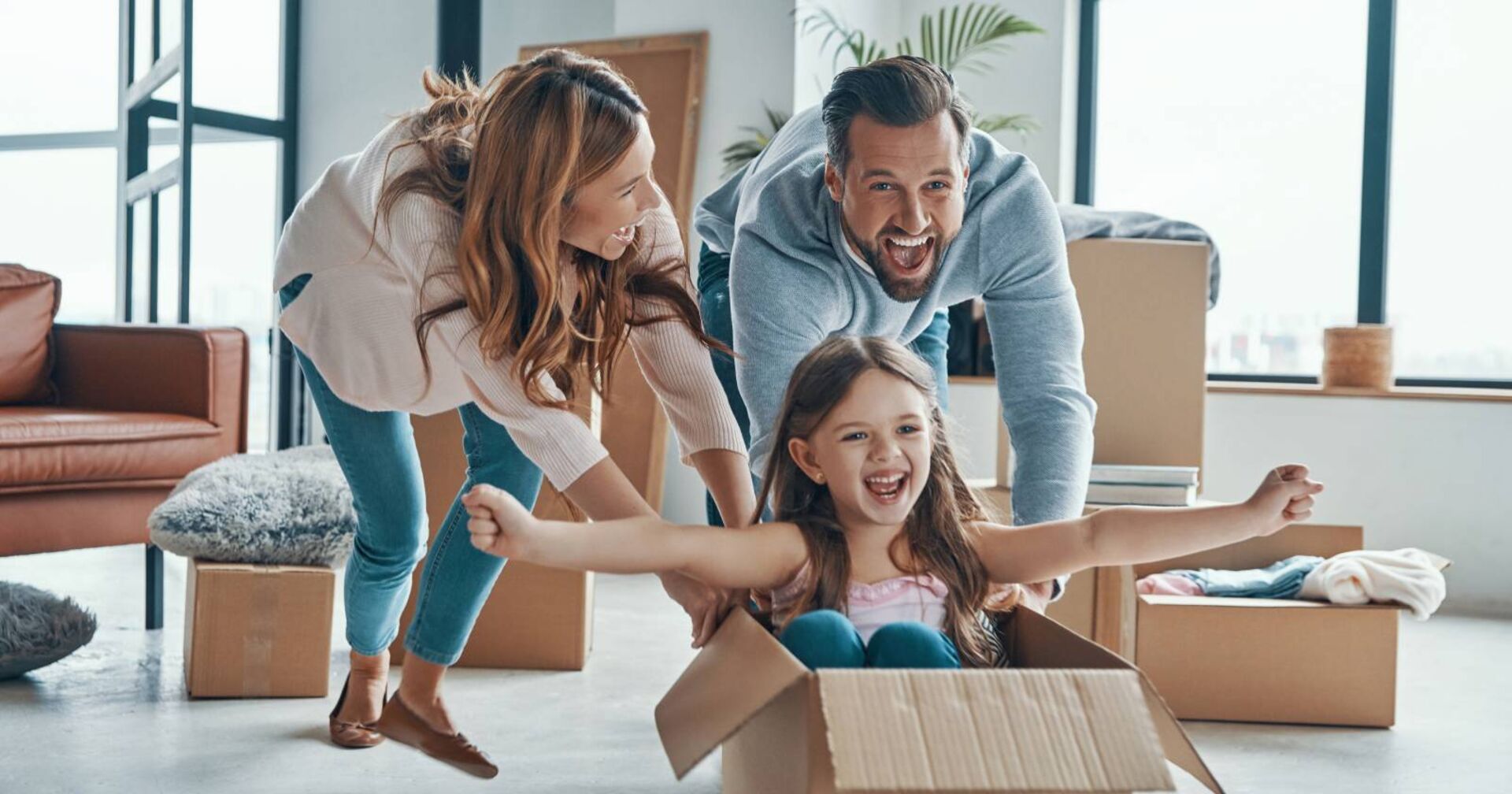 Junge Familie beim Umziehen, deren Kind gerade in einem Umzugskarton sitzt
