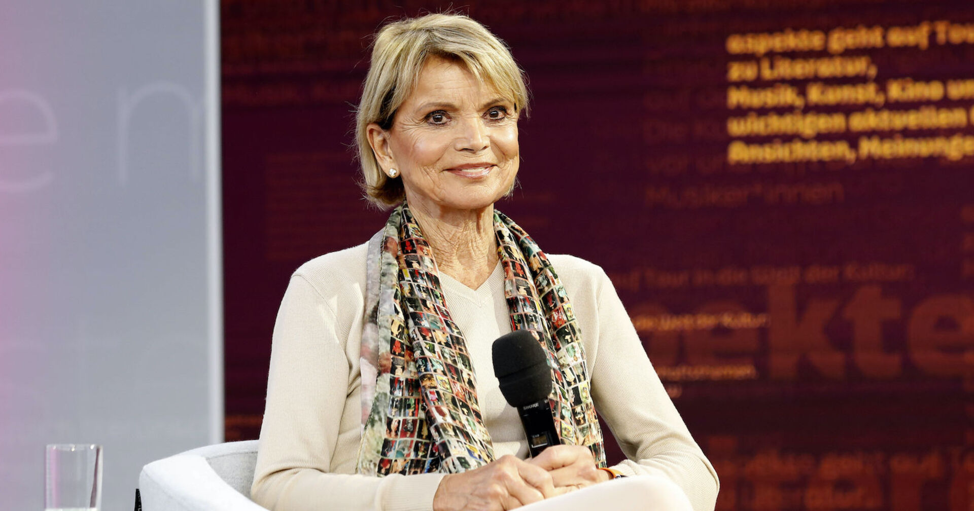 Uschi Glas mit einem beigen Outfit und einem Schal.