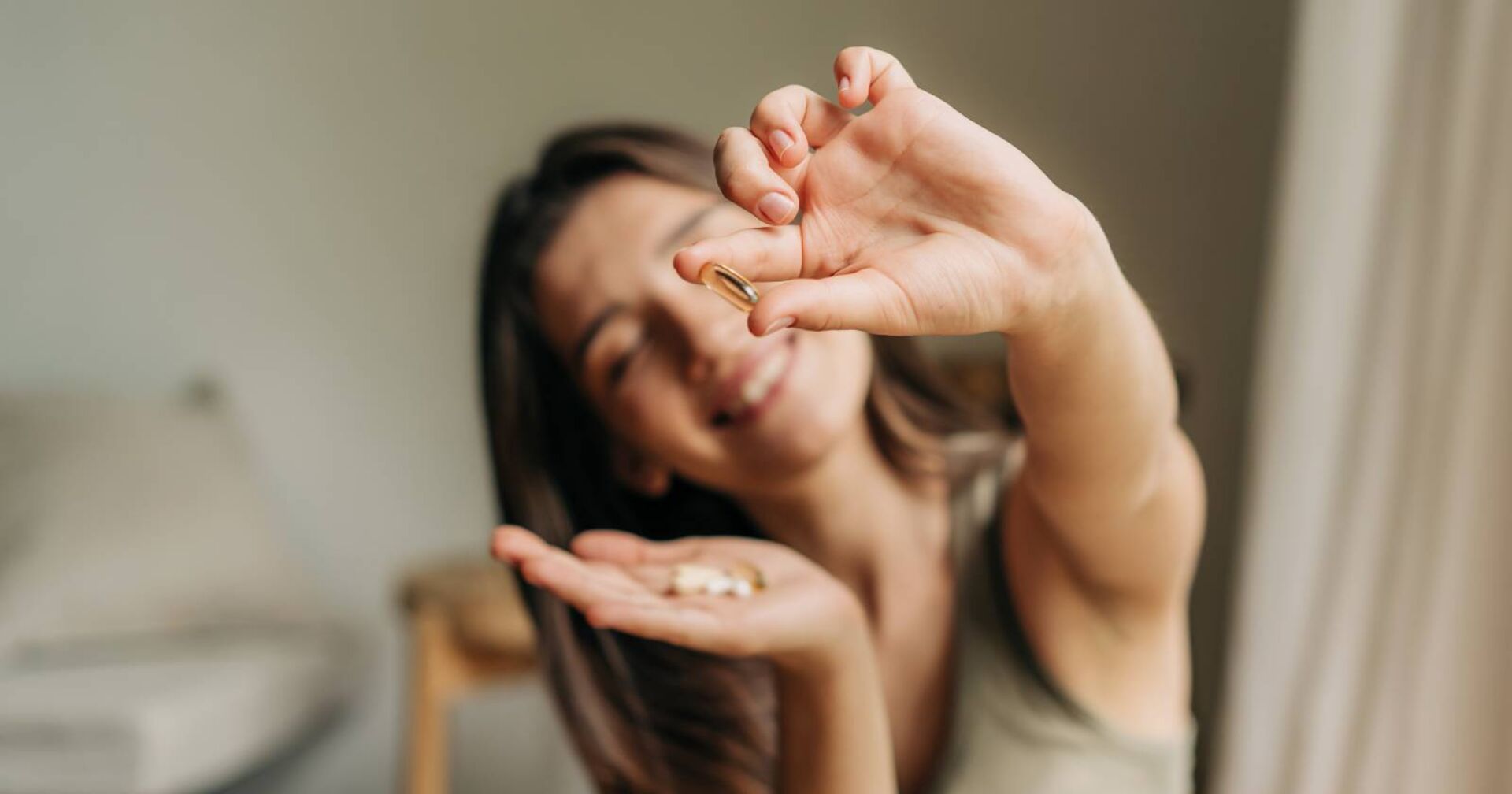Frau hält dem Betrachter eine Hartkapsel mit einem Vitaminpräparat entgegen