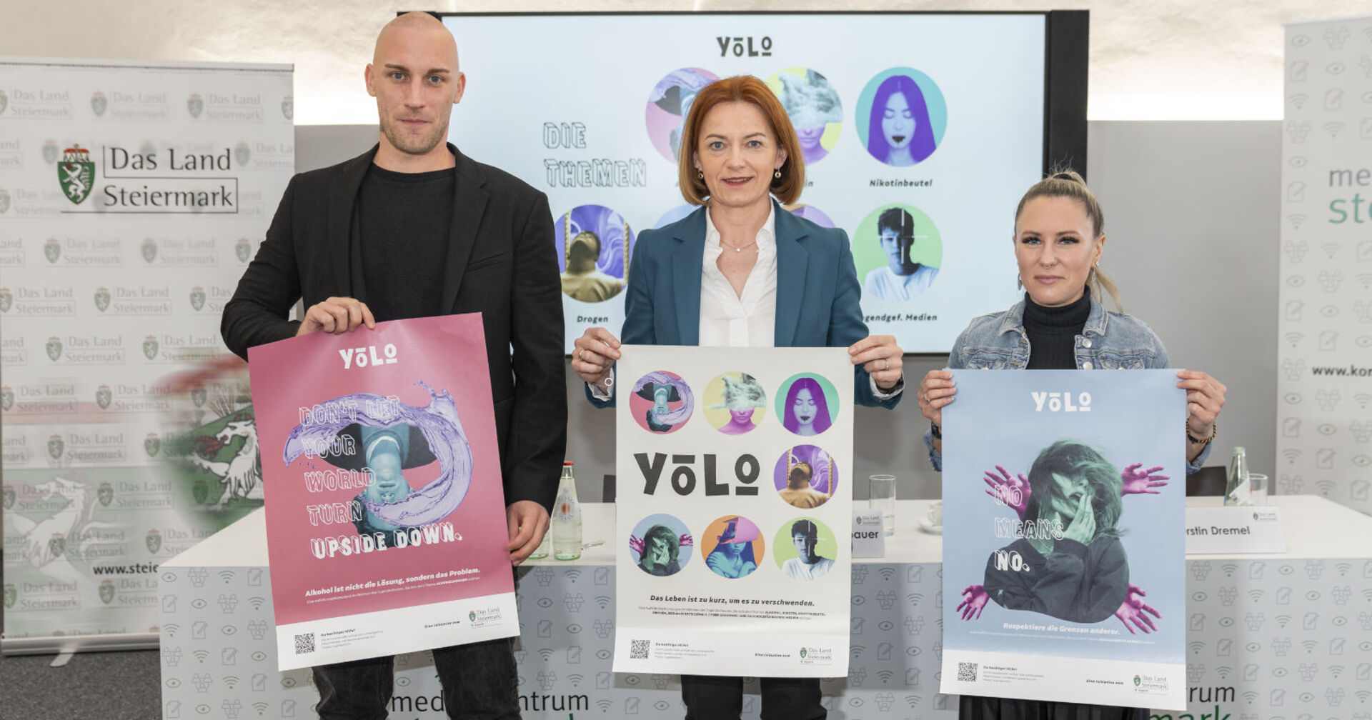 Mann und zwei Frauen stehen nebeneinander und präsenteren Plakate