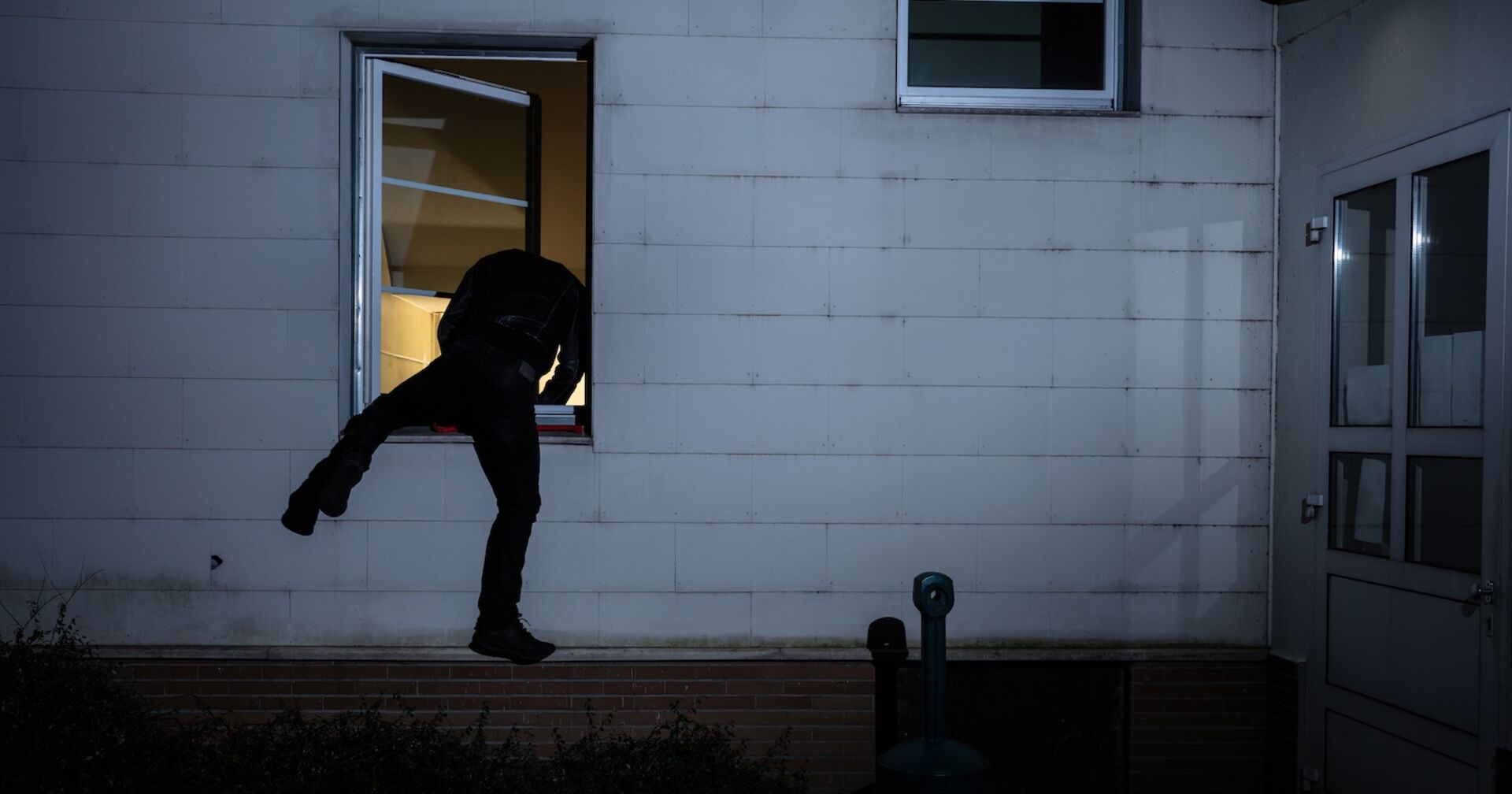 Ein Einbrecher klettert über ein Fenster in ein Haus.