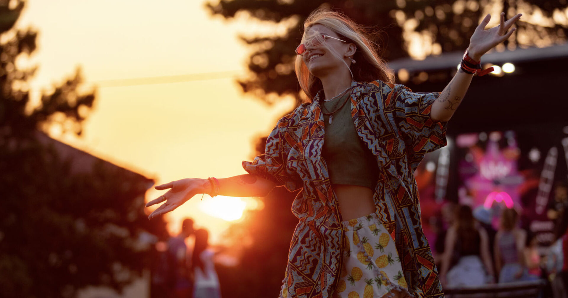 Eine blonde Frau mit Sonnenbrille tanzt in der untergehenden Sonne auf einem Festival