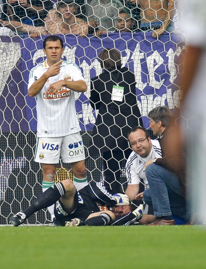 Georg Koch liegt mit schmerzverzerrtem Gesicht am Spielfeld, Ärzte betreuen ihn. Ein Rapidspieler gibt das Zeichen für einen Wechsel.