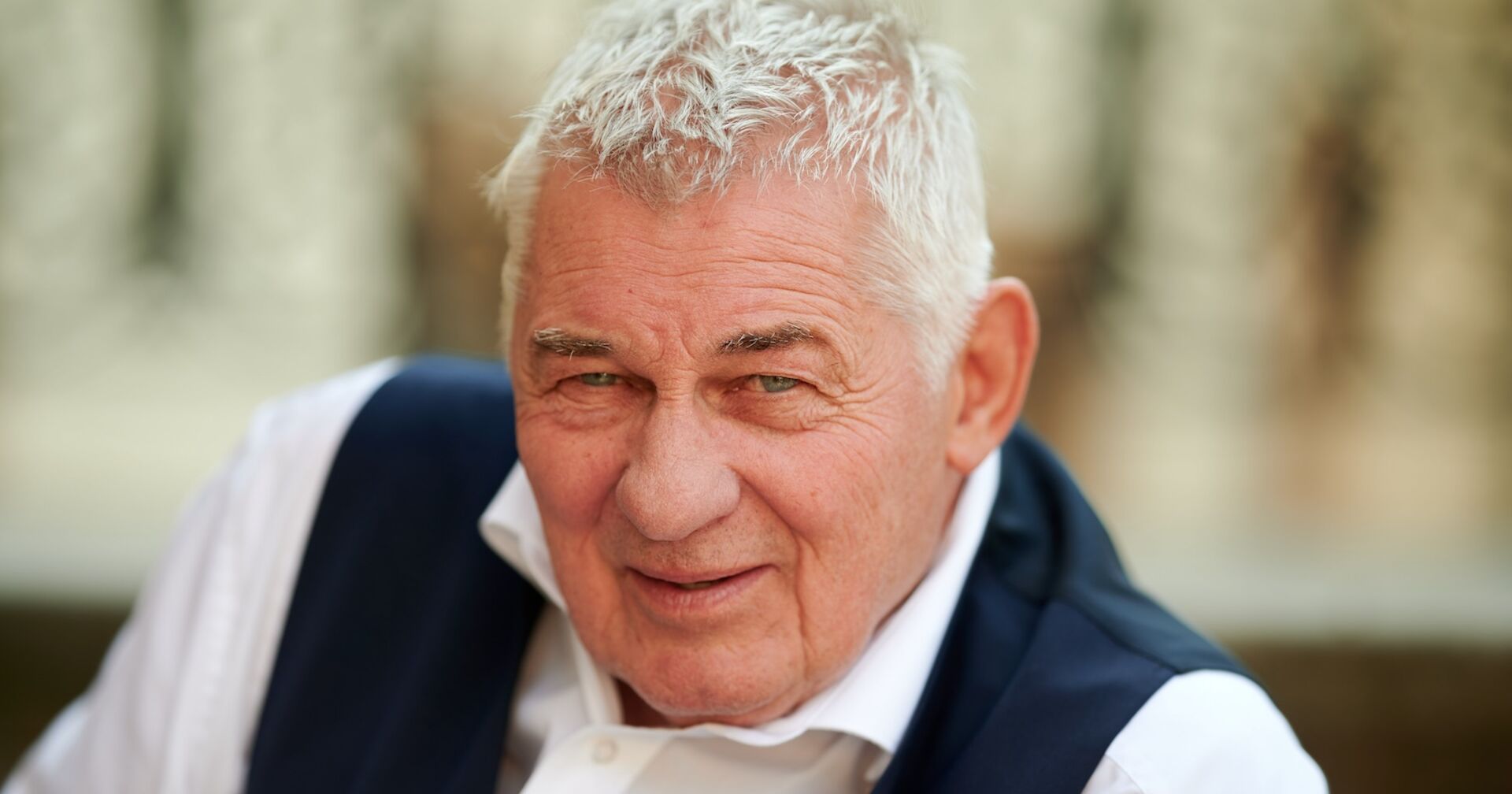 Heinz Hoenig mit einem weißen Hemd und einer blauen Weste.