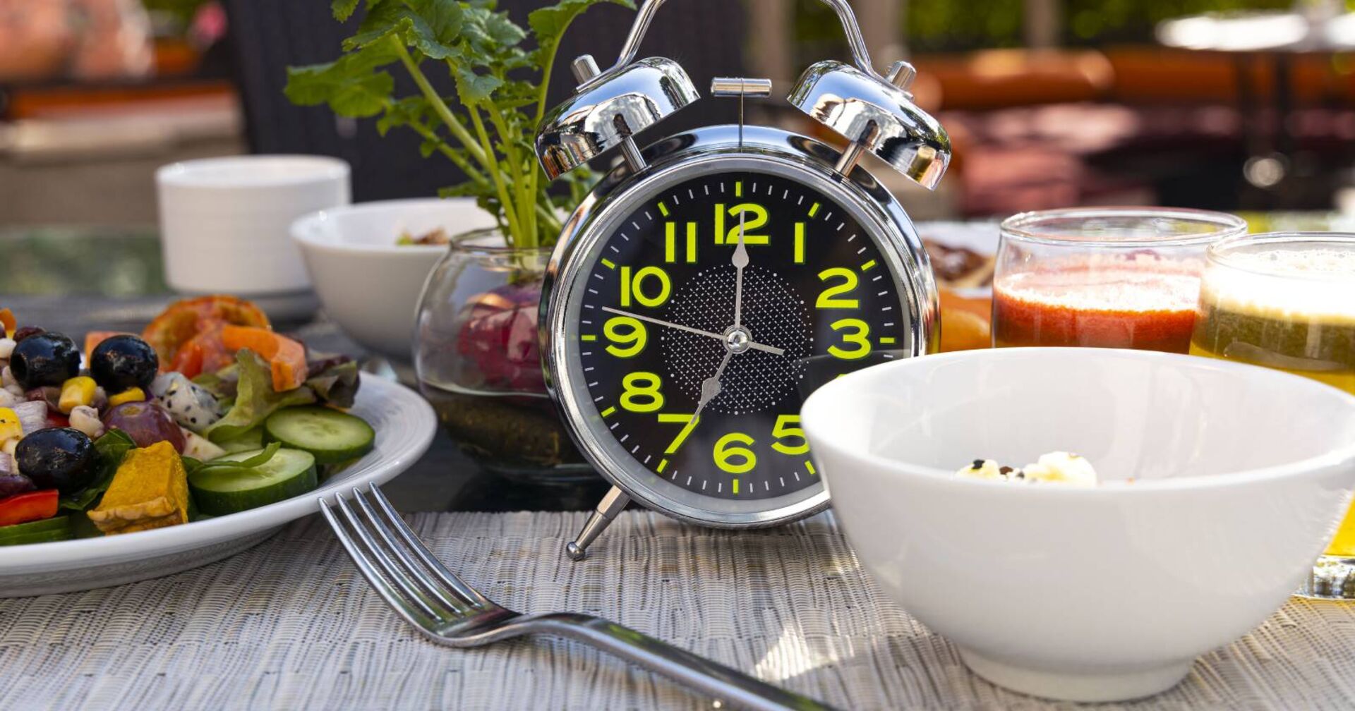 Konzept &quot;Intervallfasten&quot; mit einem Wecker beim Frühstück mit gesunder Ernährung