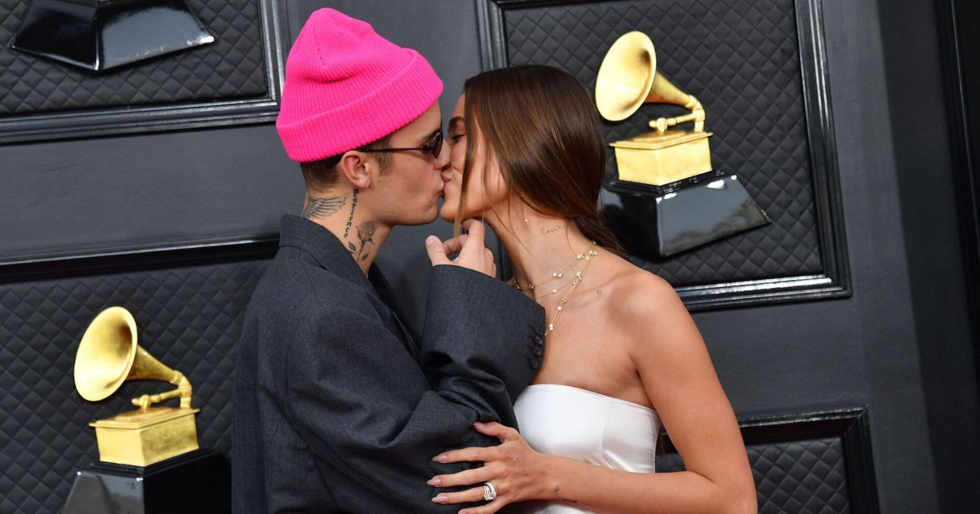 Justin Bieber trägt eine pinke Mütze und küsst seine Frau Hailey auf dem Red Carpet.