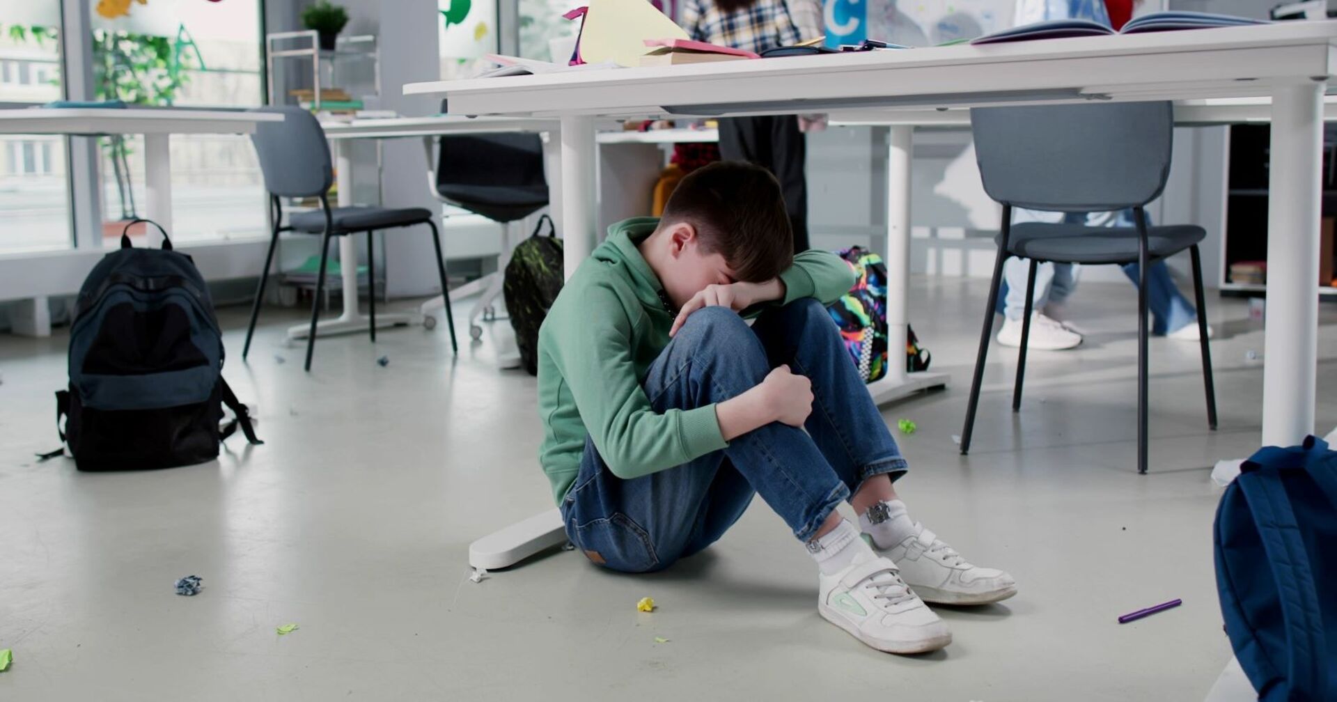 Ein Bub sitzt weinend auf dem Boden im Klassenzimmer.