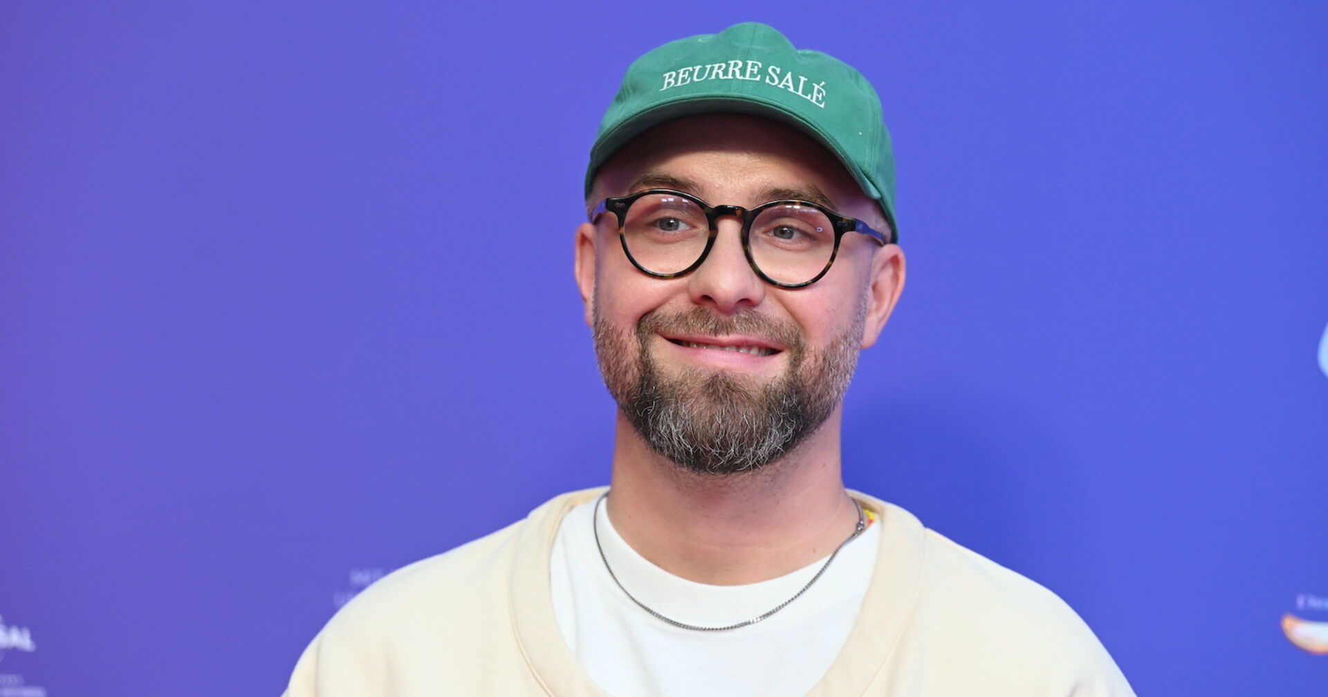 Mark Forster mit einer grünen Kappe und einem weißen Pullover und einer silbernen Kette.