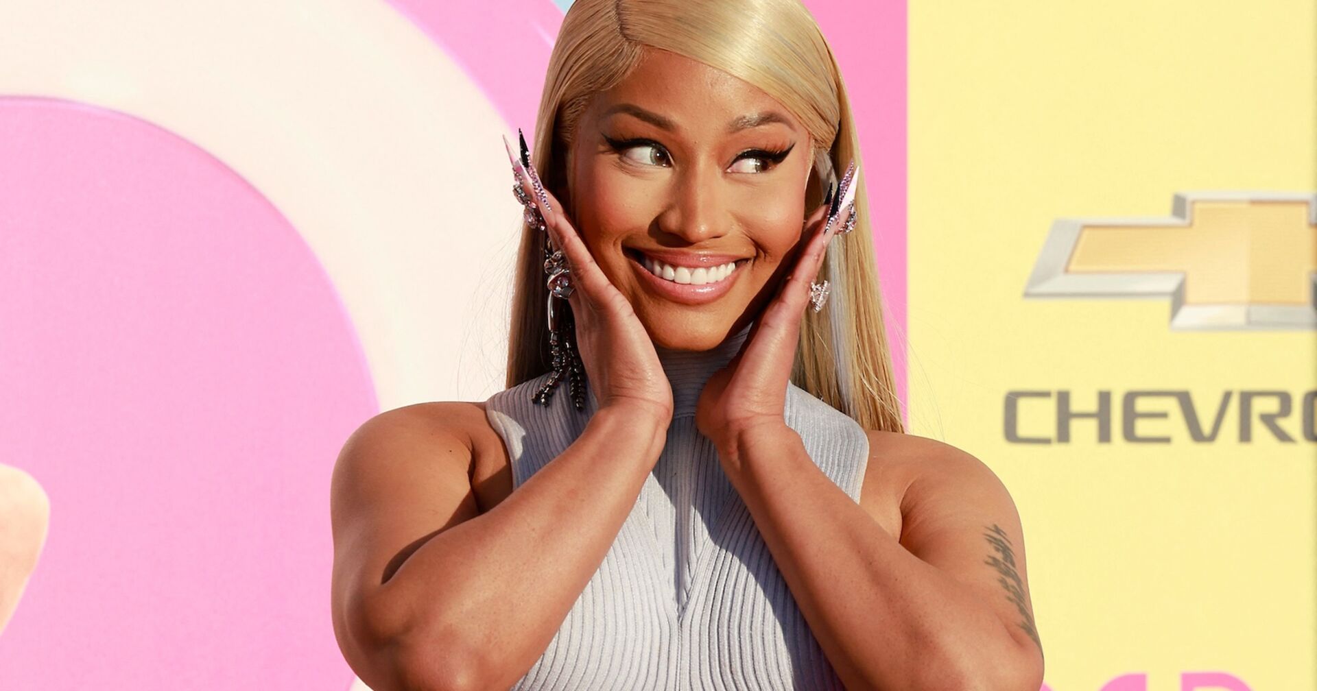Nicki Minaj mit blonden glatten Haaren und einem grauen Oberteil.
