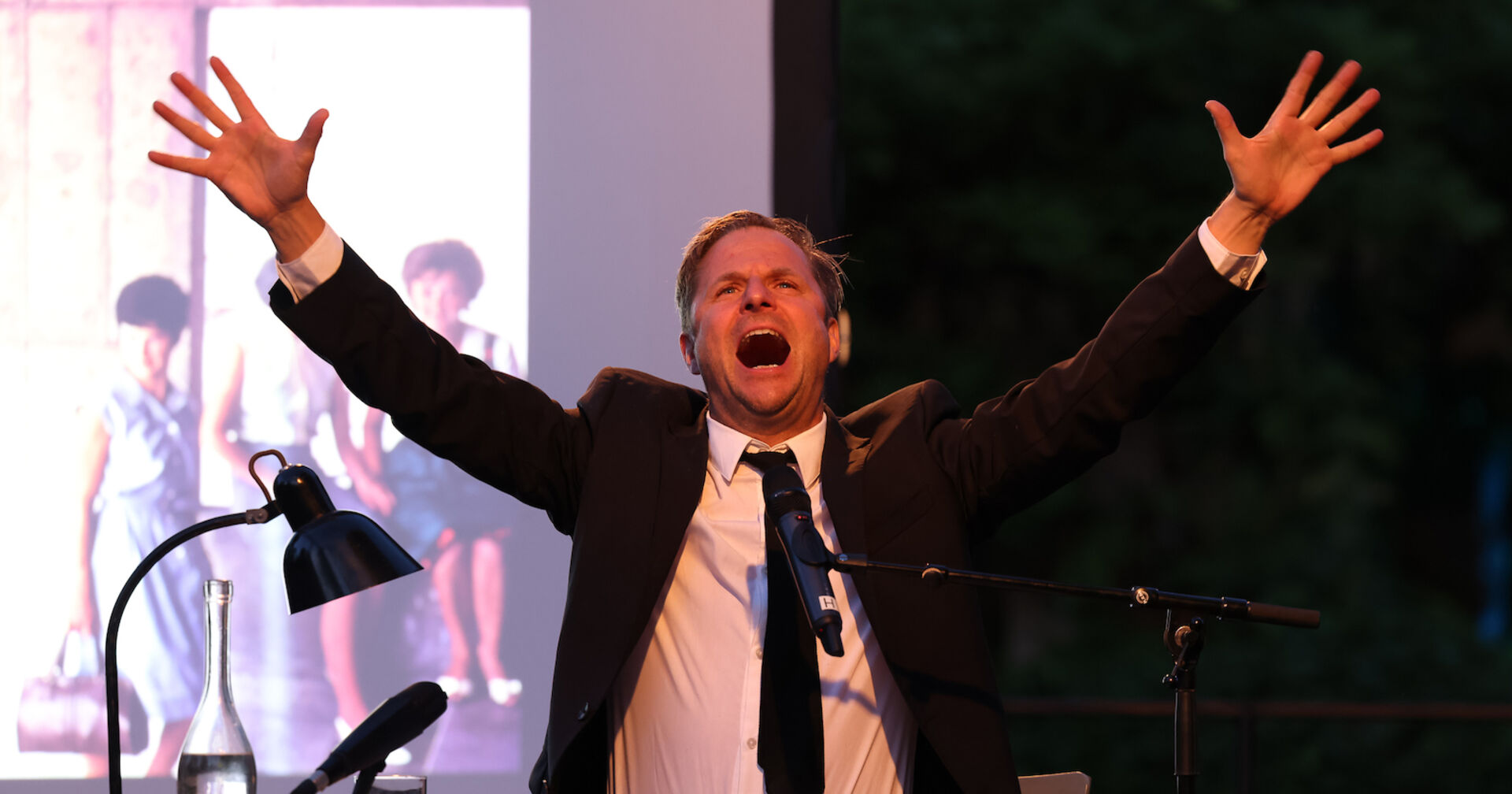 Philipp Hochmair mit einem schwarzen Anzug und einer schwarzen Krawatte auf der Bühne.