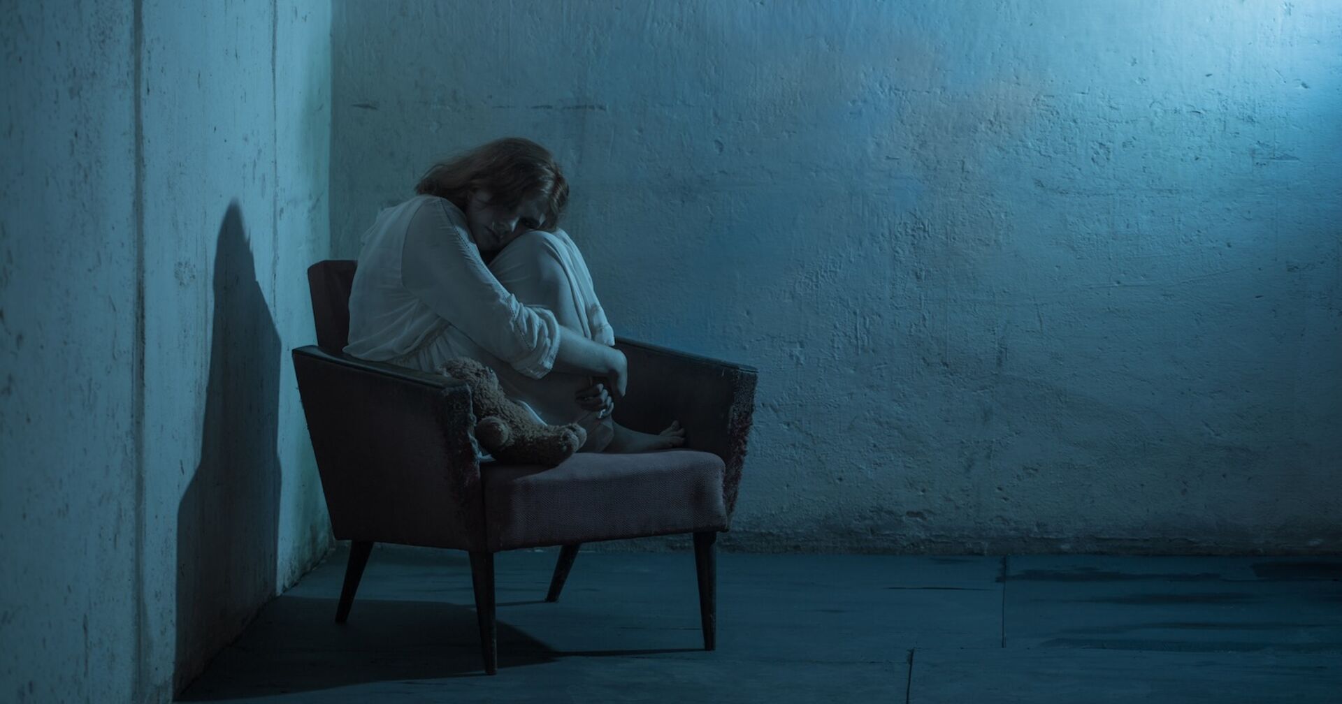 Ein Mädchen sitzt traurig in einem dunklen Raum.