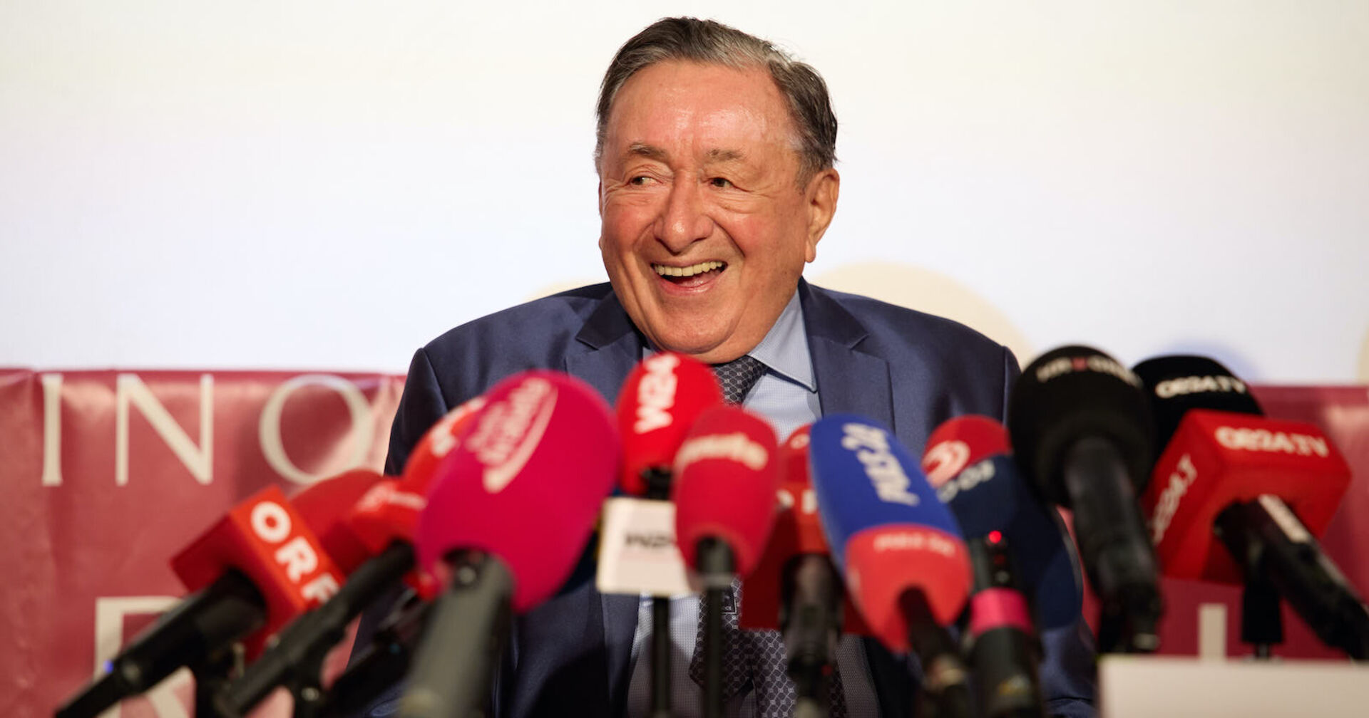 Richard Lugner lachend vor Mikrofonen.