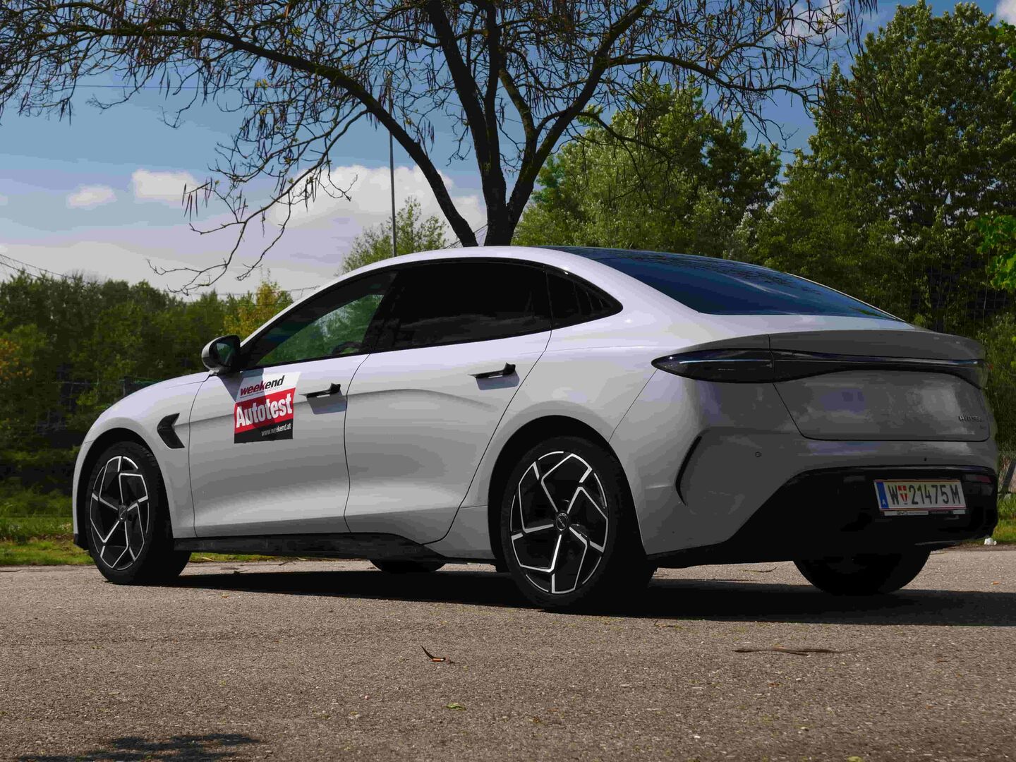 Ein weißer BYD Seal 3.85 von der Seite: Das chinesische E-Auto steht im Sonnenlicht auf einem asphaltiertem Parkplatz. Im Hintergrund sind einige Laubbäume zu sehen.