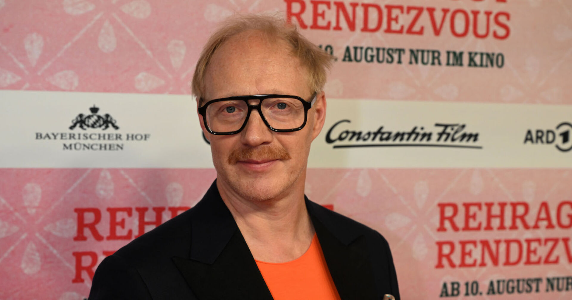 Simon Schwarz mit einem schwarzen Sakko und einem orangenen Hemd.