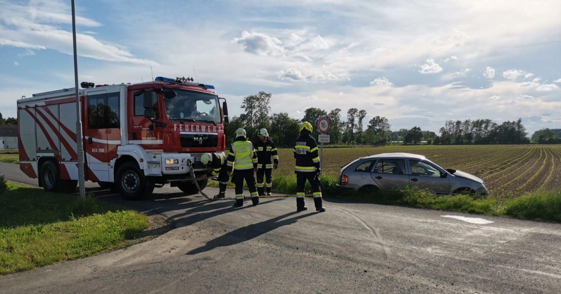 Ein Feuerwehrauto, Einsatzkräfte und ein Pkw im Straßengraben