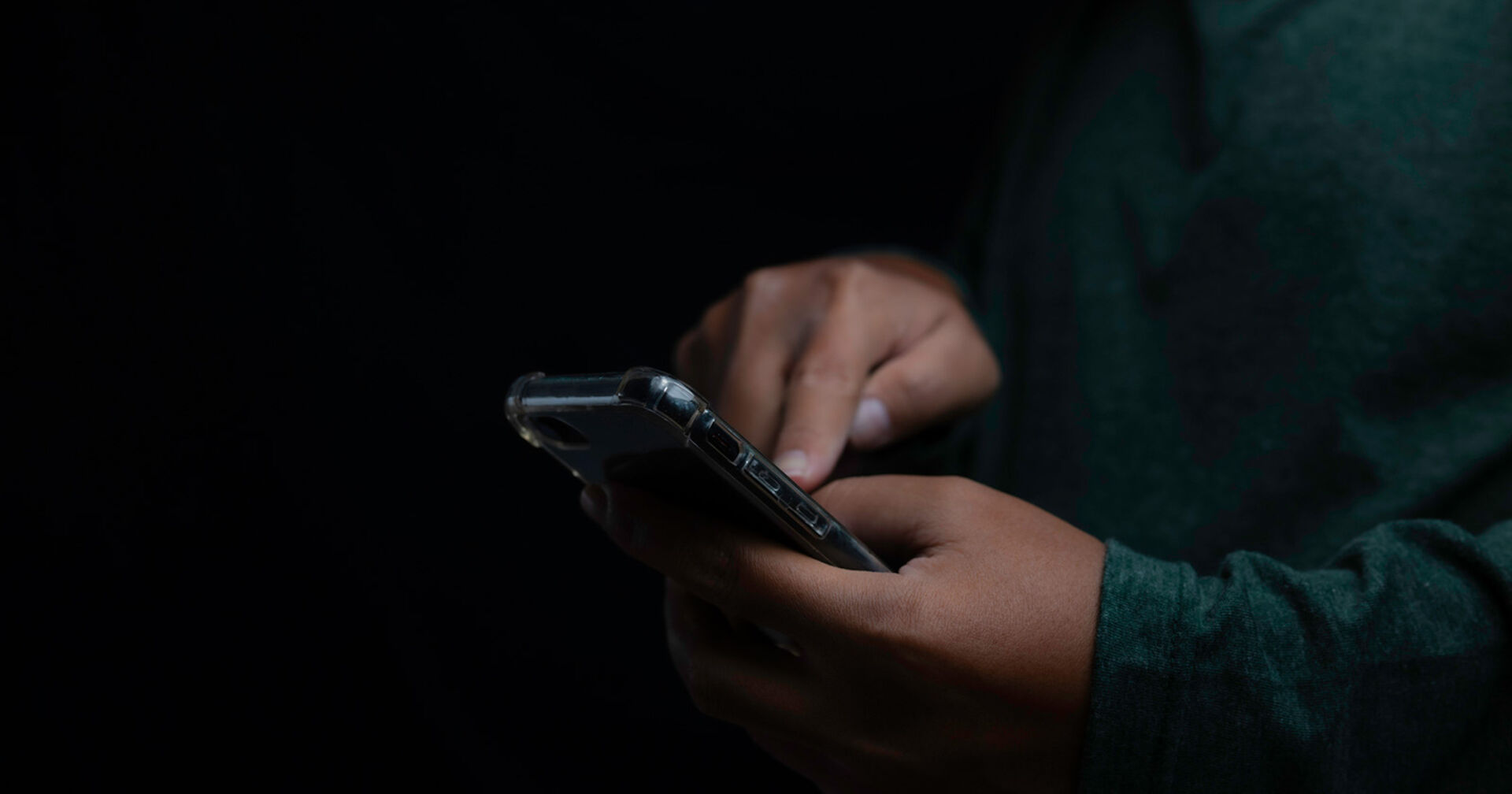 Mann vor einem dunklen Hintergrund tippt etwas in sein Smartphone ein.