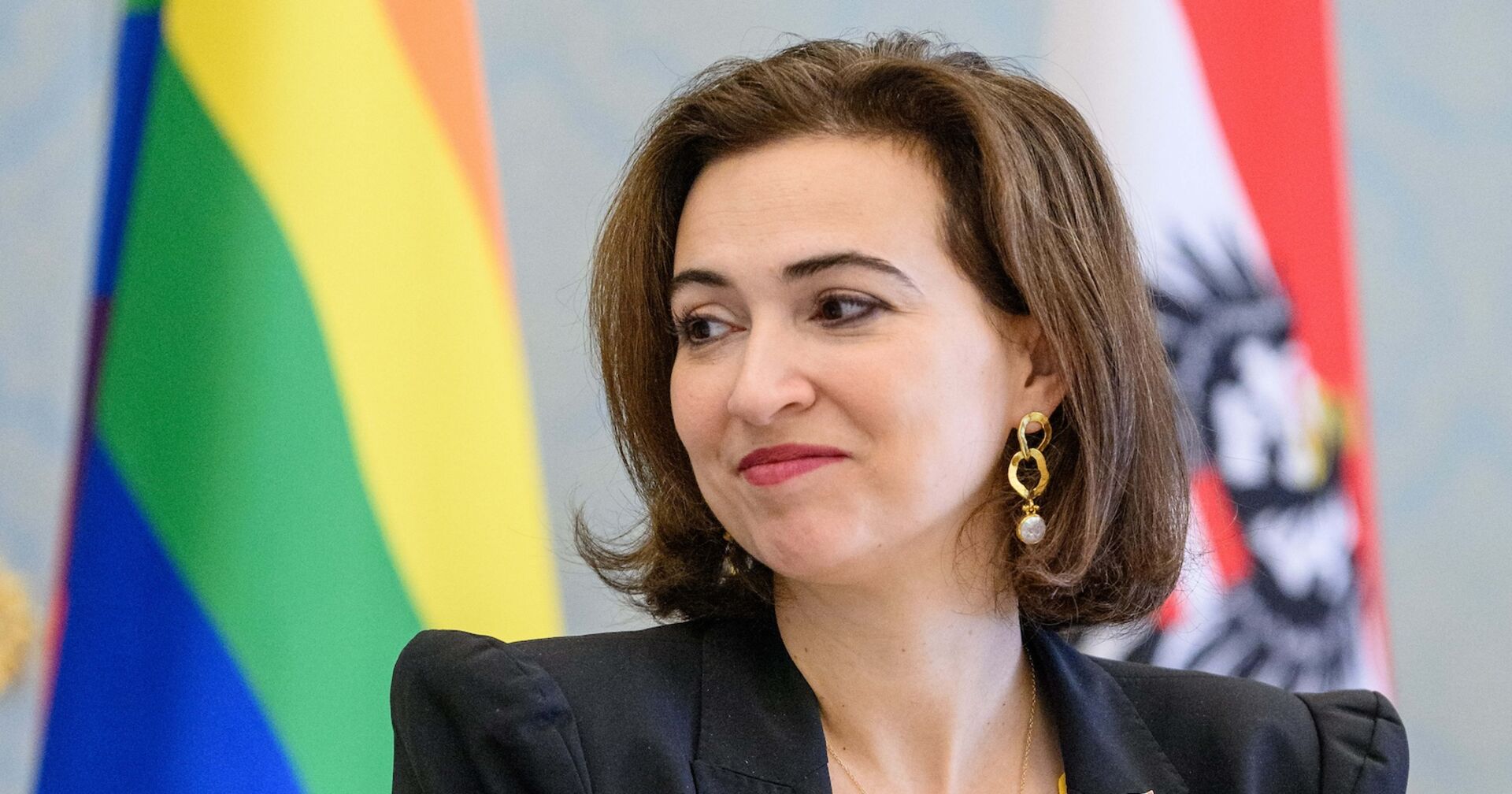 Justizministerin Alma Zadic von den Grünen im Porträt, hinter ihr eine Regenbogen- und eine Österreich-Fahne