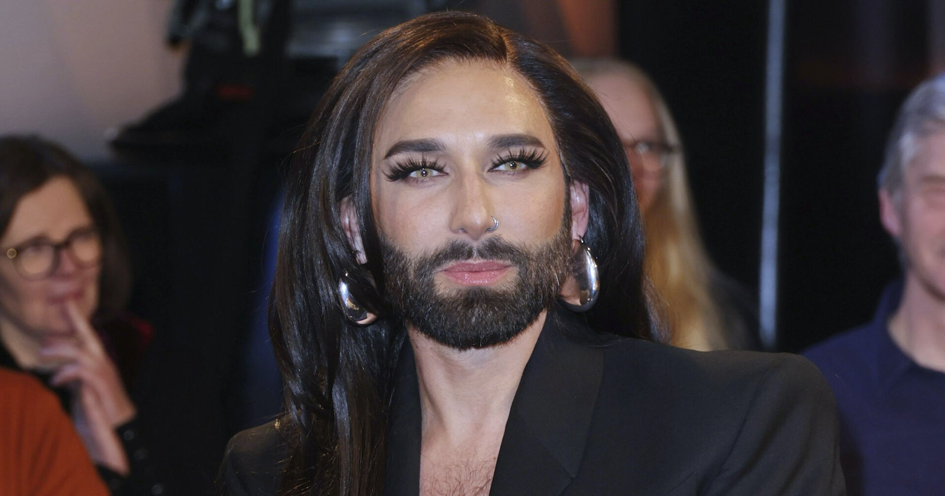 Conchita Wurst mit einem schwarzen Sakko und langen schwarzen Haaren.