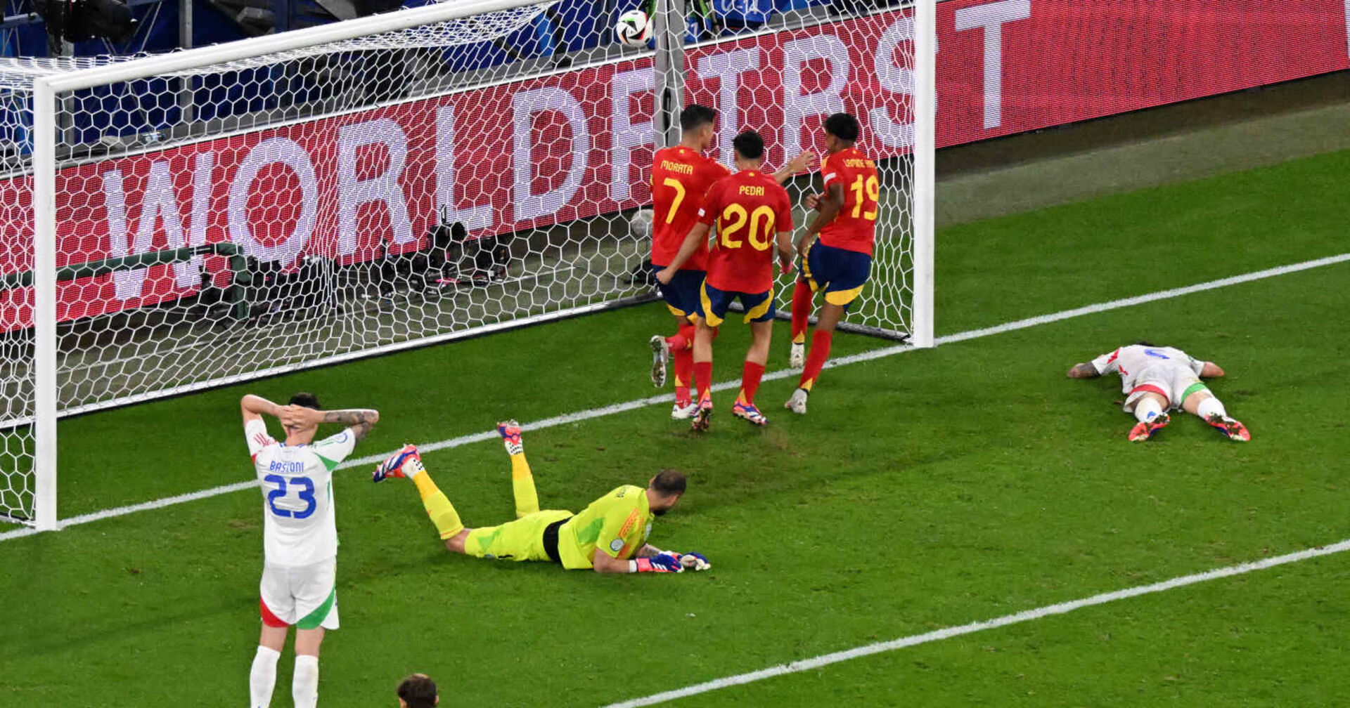 Vor dem Tor eines Fußballfeldes liegen zwei Männer, drei jubeln daneben