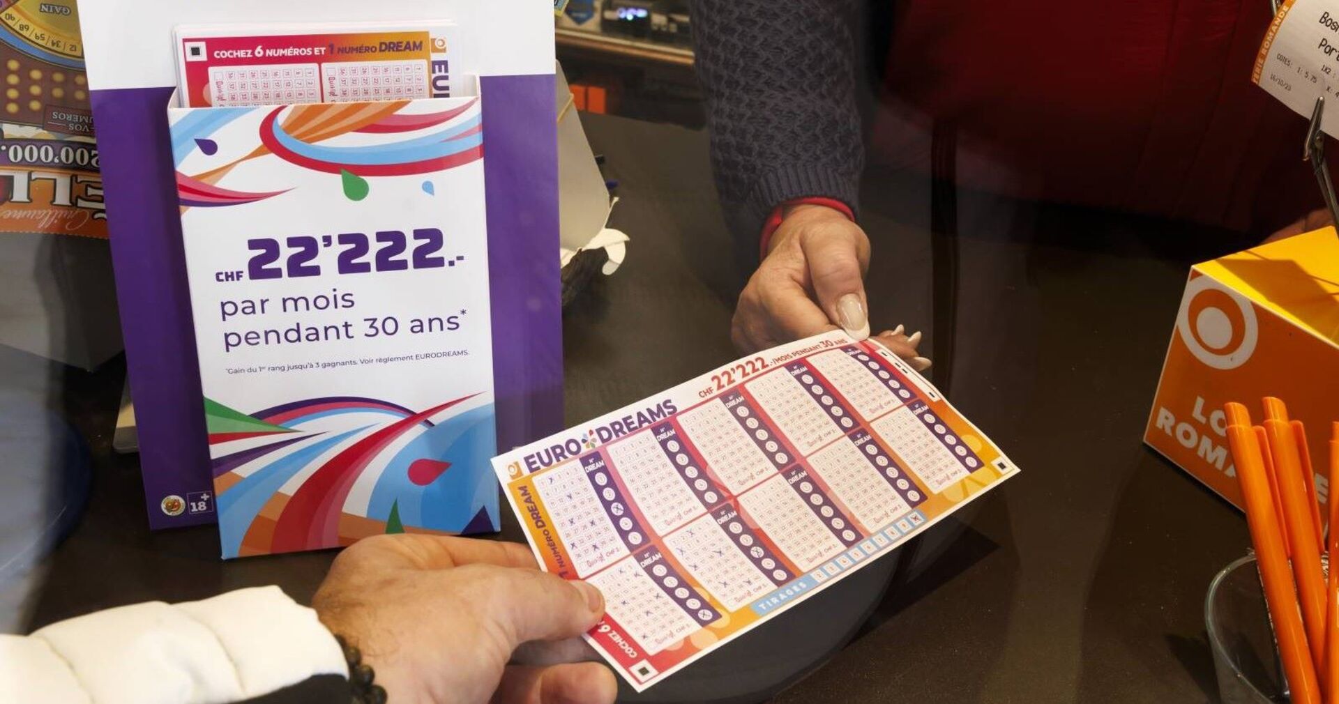 Jemand gibt einen ausgefüllten EuroDreams-Tippschein ab.