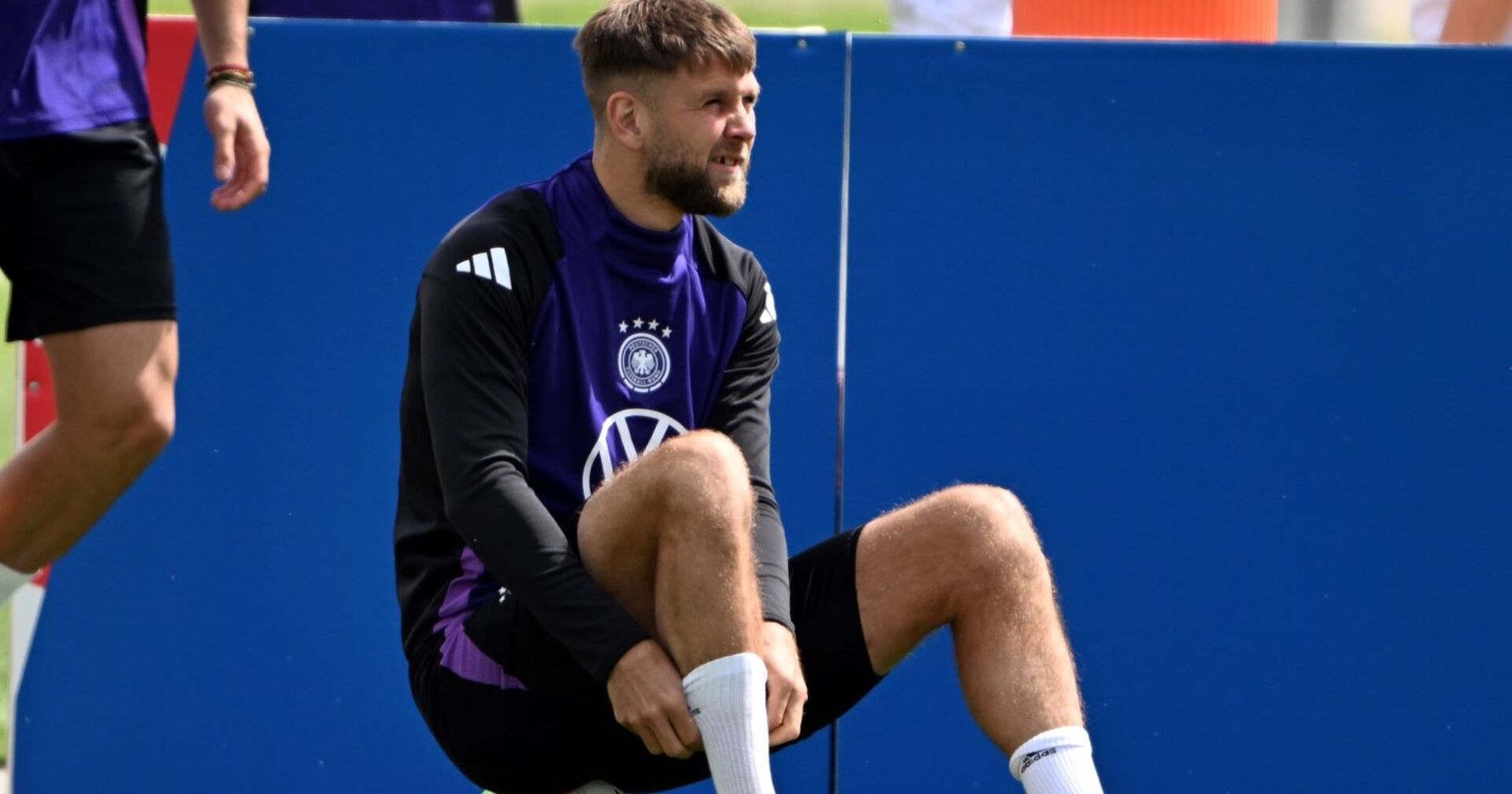 Niclas Füllkrug sitzt am Rasen auf einem Fußball.