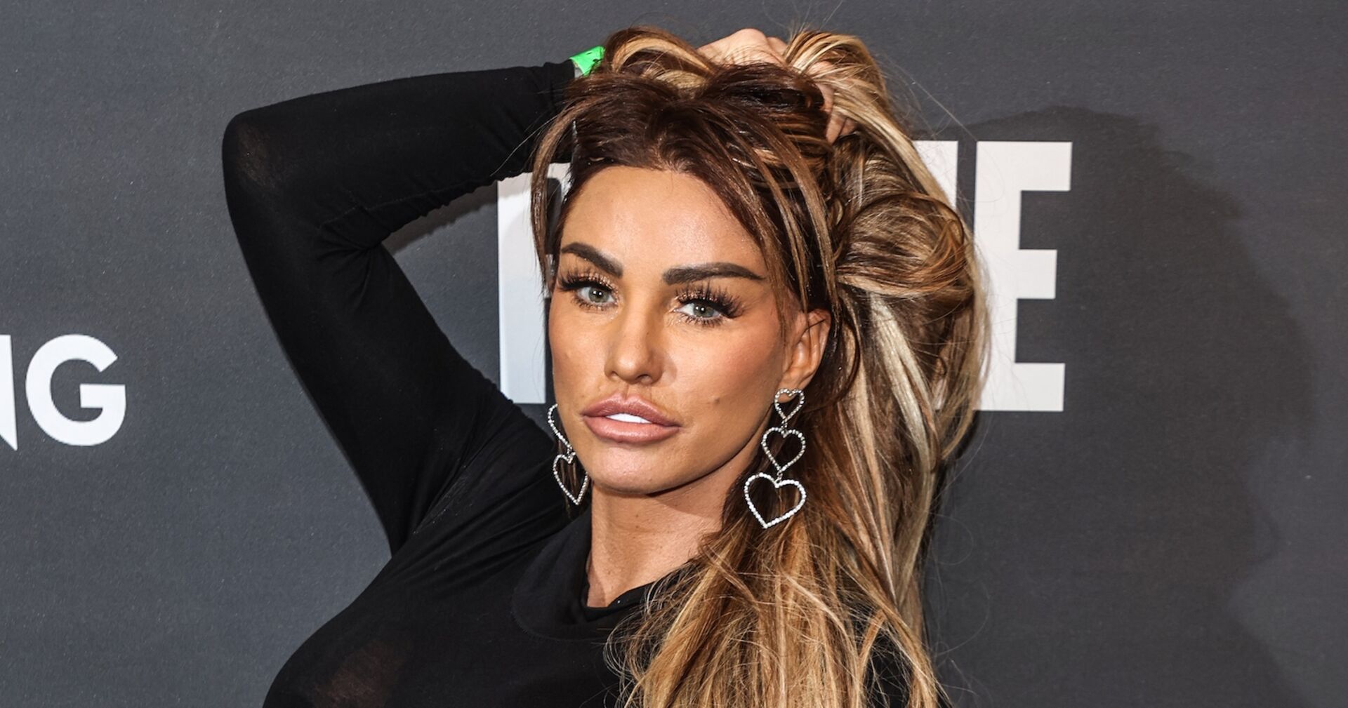 Katie Price mit hochgehaltenen langen Haaren und Ohrringen in Herzform.