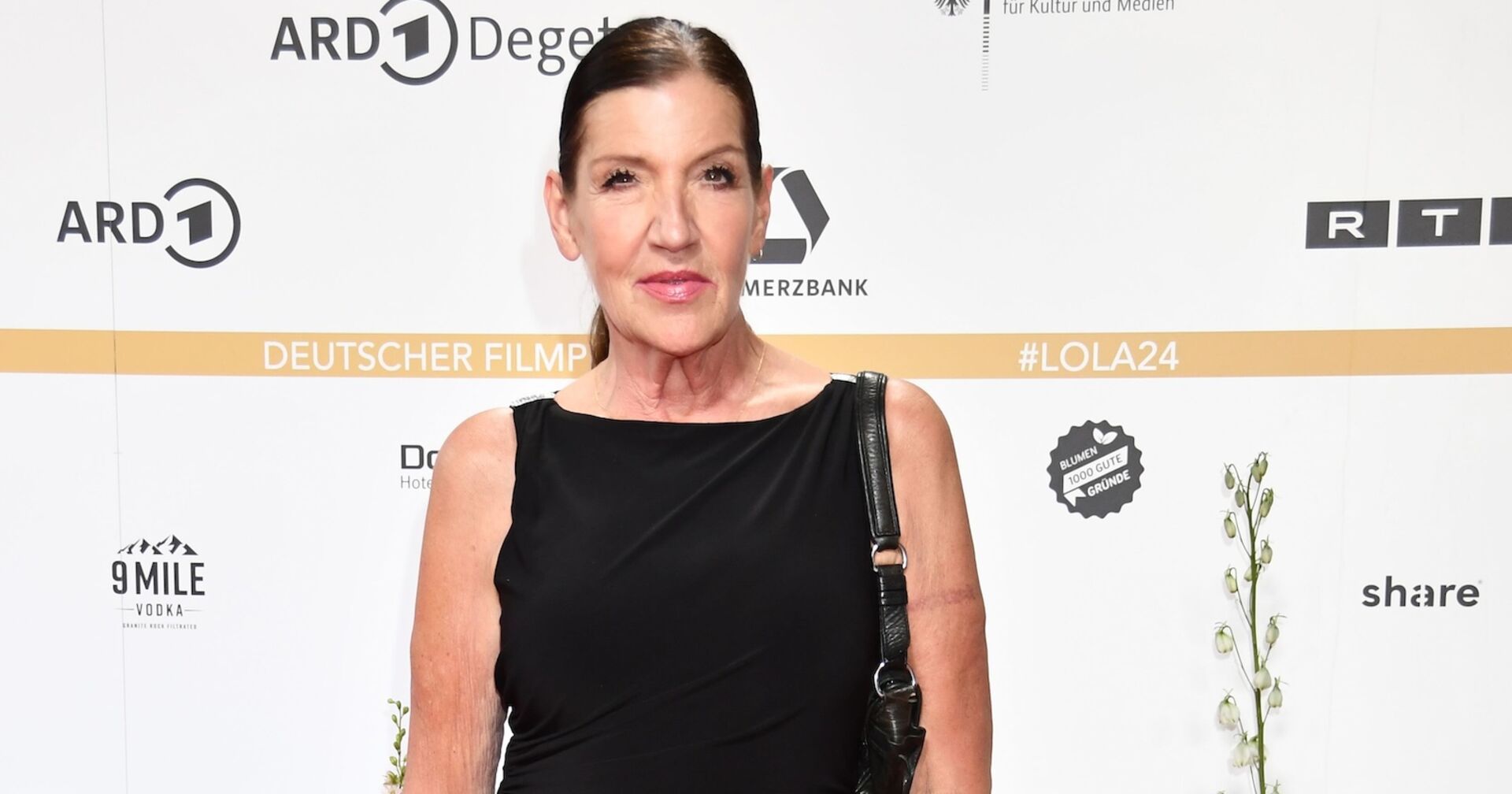 Katy Karrenbauer mit einem schwarzen Outfit vor einer Fotowand.