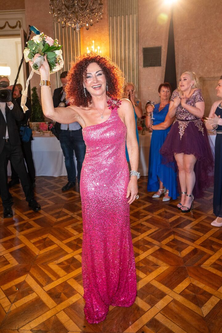 Christina Lugner in einem pinken bodenlangen Kleid mit einem Brautstrauss.