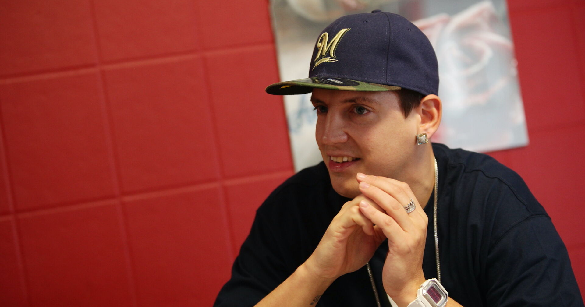 Money Boy mit einer schwarzen Kappe und einem schwarzen T-shirt vor einem roten Hintergrund.